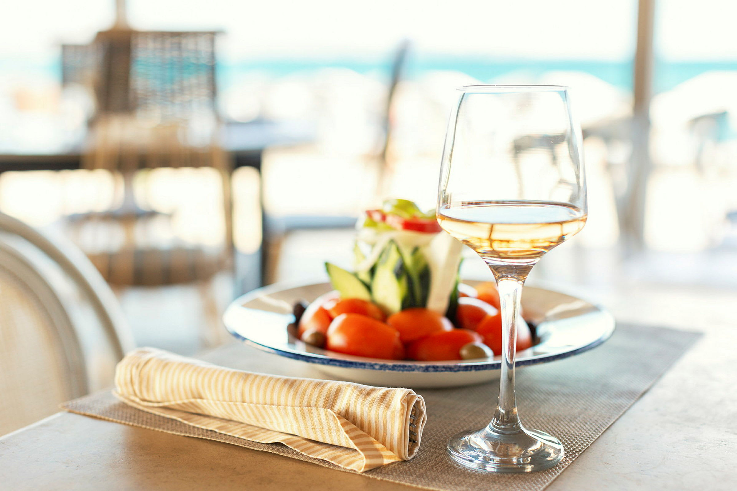 Ett glas vin står bredvid en tallrik med färsk sallad och tomater på ett dukat bord. (AI-genererad text)