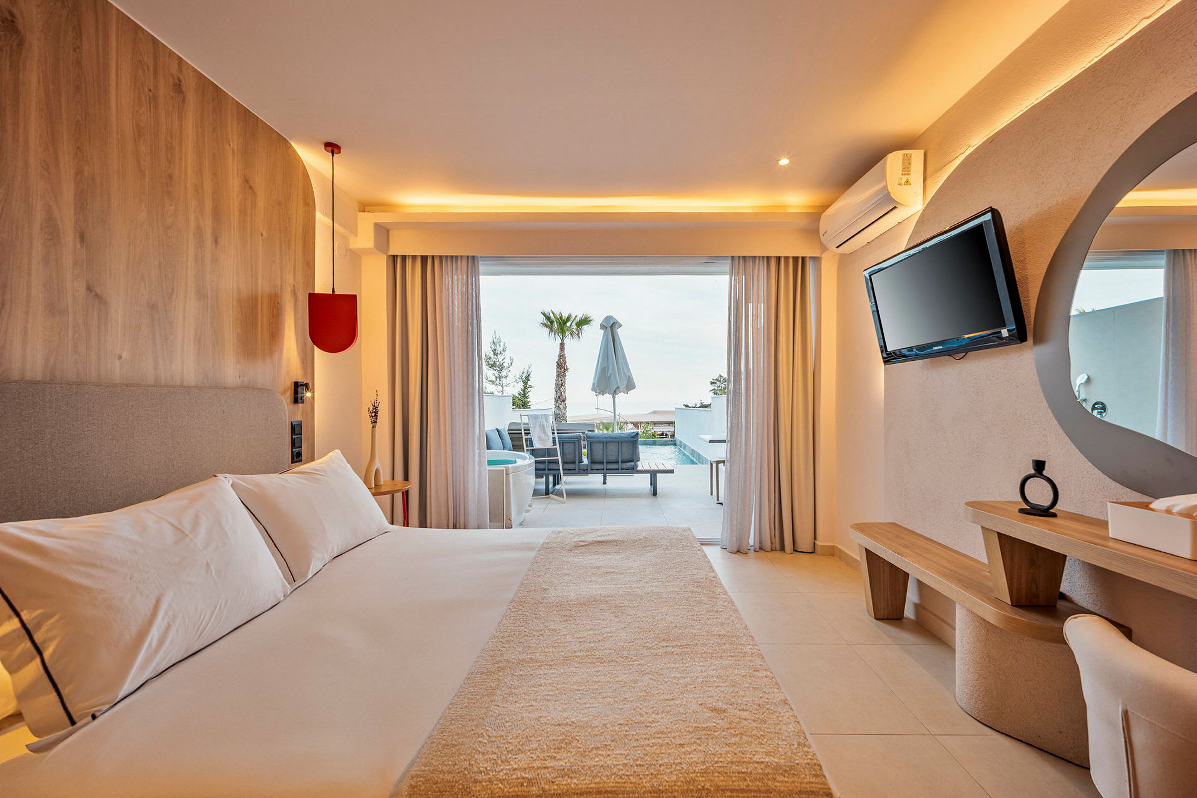 Ett ljust hotellrum med en bred säng, modern inredning och en öppen dörr som leder ut till en möblerad terrass med utsikt över en pool och palmträd. (AI-genererad text)
