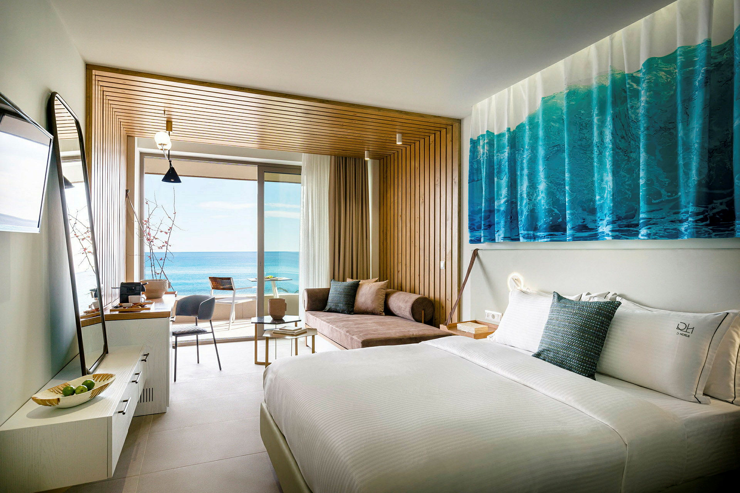 Ett hotellrum med en vit säng, en soffa och ett bord, och en balkong med utsikt över havet. (AI-genererad text)