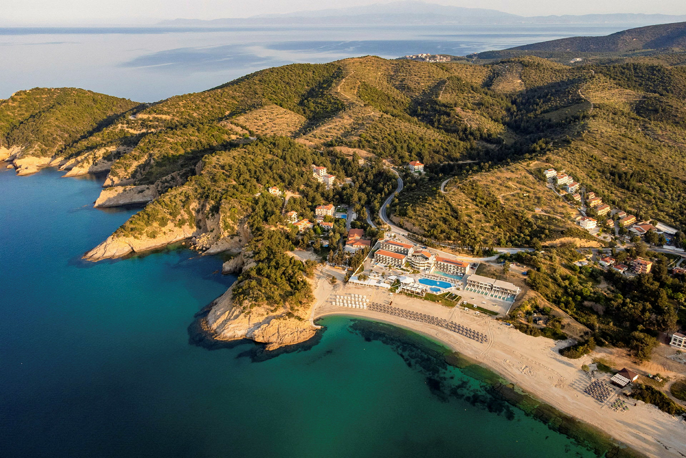 Flygfoto av en kust med sandstrand, turkost vatten och grönskande kullar. (AI-genererad text)
