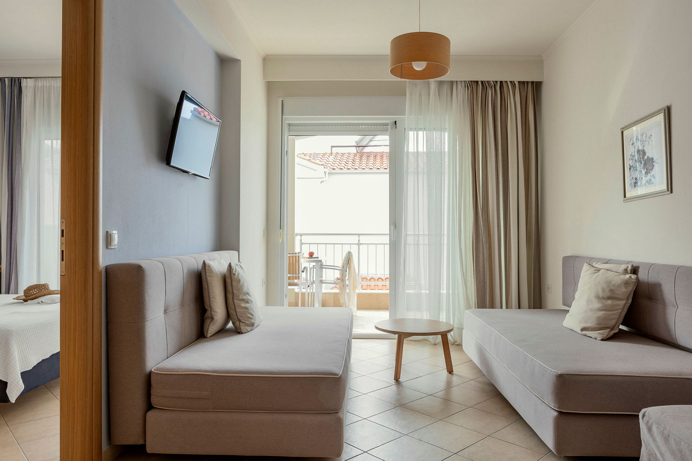 Ett hotellrum med sittmöbler, en TV på väggen och en balkong i bakgrunden. (AI-genererad text)