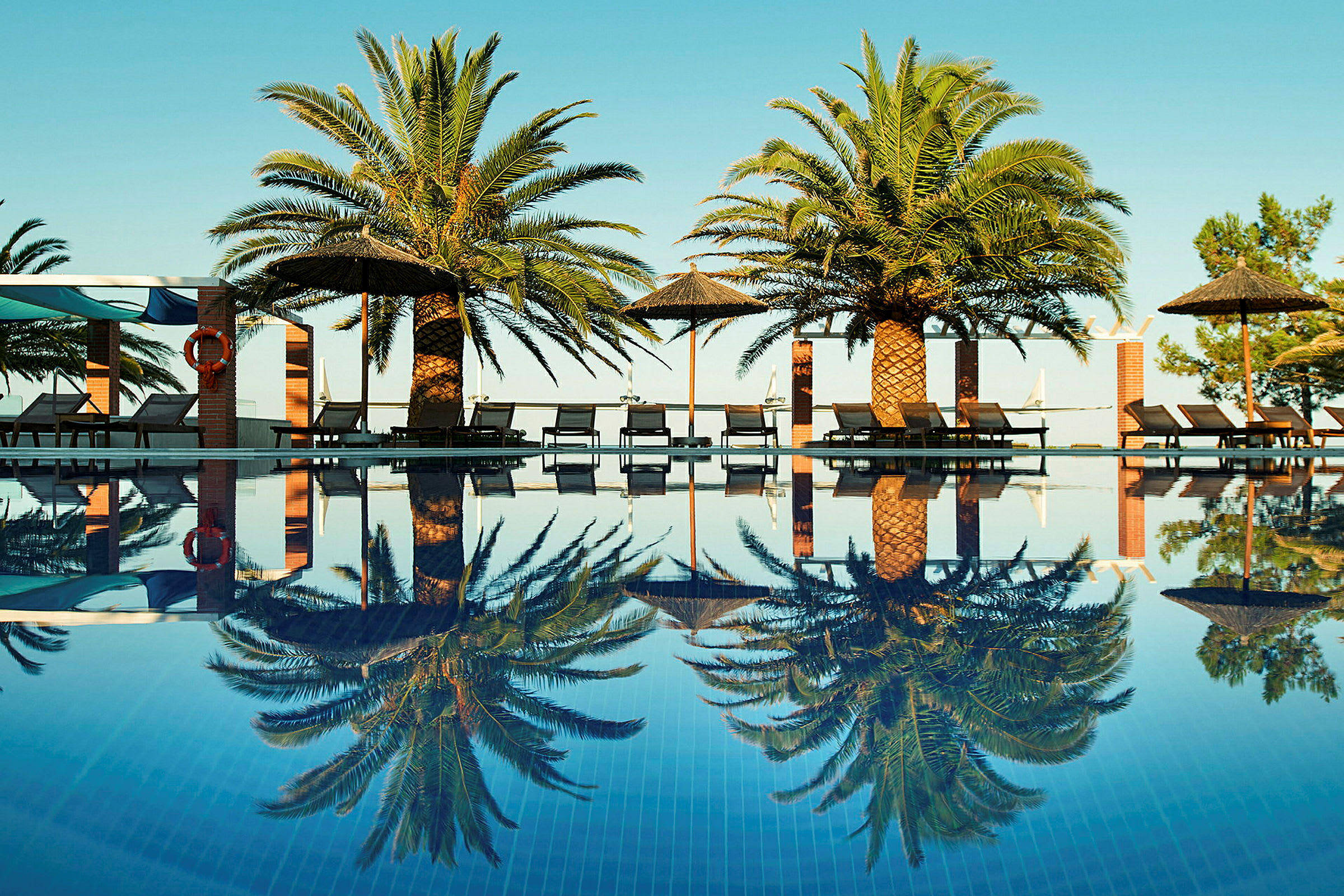 Pool med palmer och solsängar runtom, reflektioner i vattnet. (AI-genererad text)
