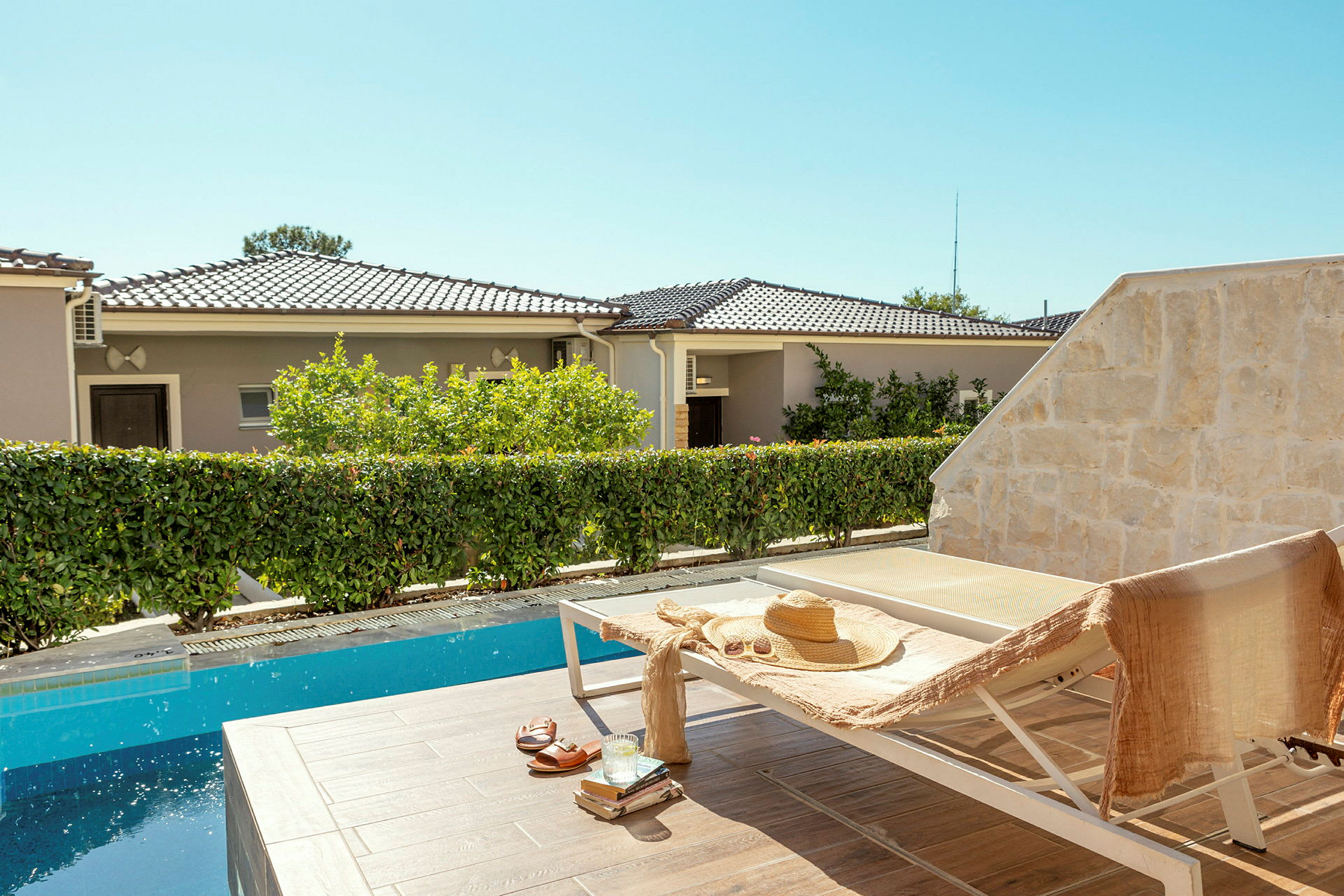 En solstol vid en pool med en stråhatt och en handduk på. I bakgrunden syns bostadshus och vegetation. (AI-genererad text)