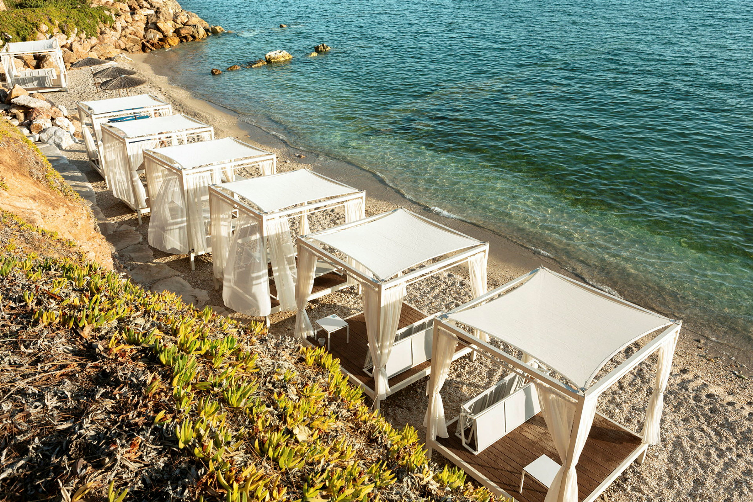 Lusthus med vita tak och gardiner vid en strand. (AI-genererad text)