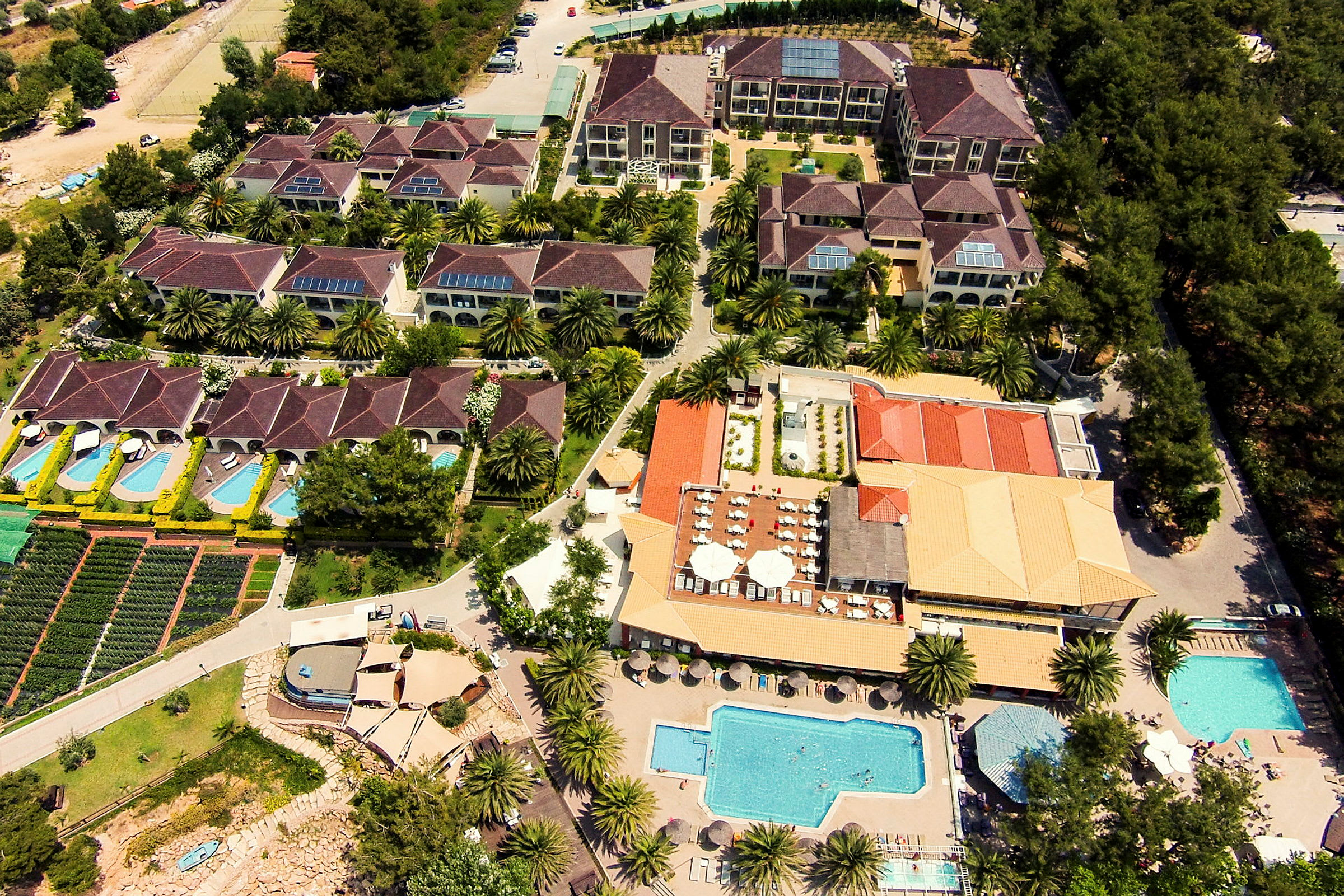 Flygbild av en hotellanläggning med flera byggnader, pooler och grönområden. (AI-genererad text)