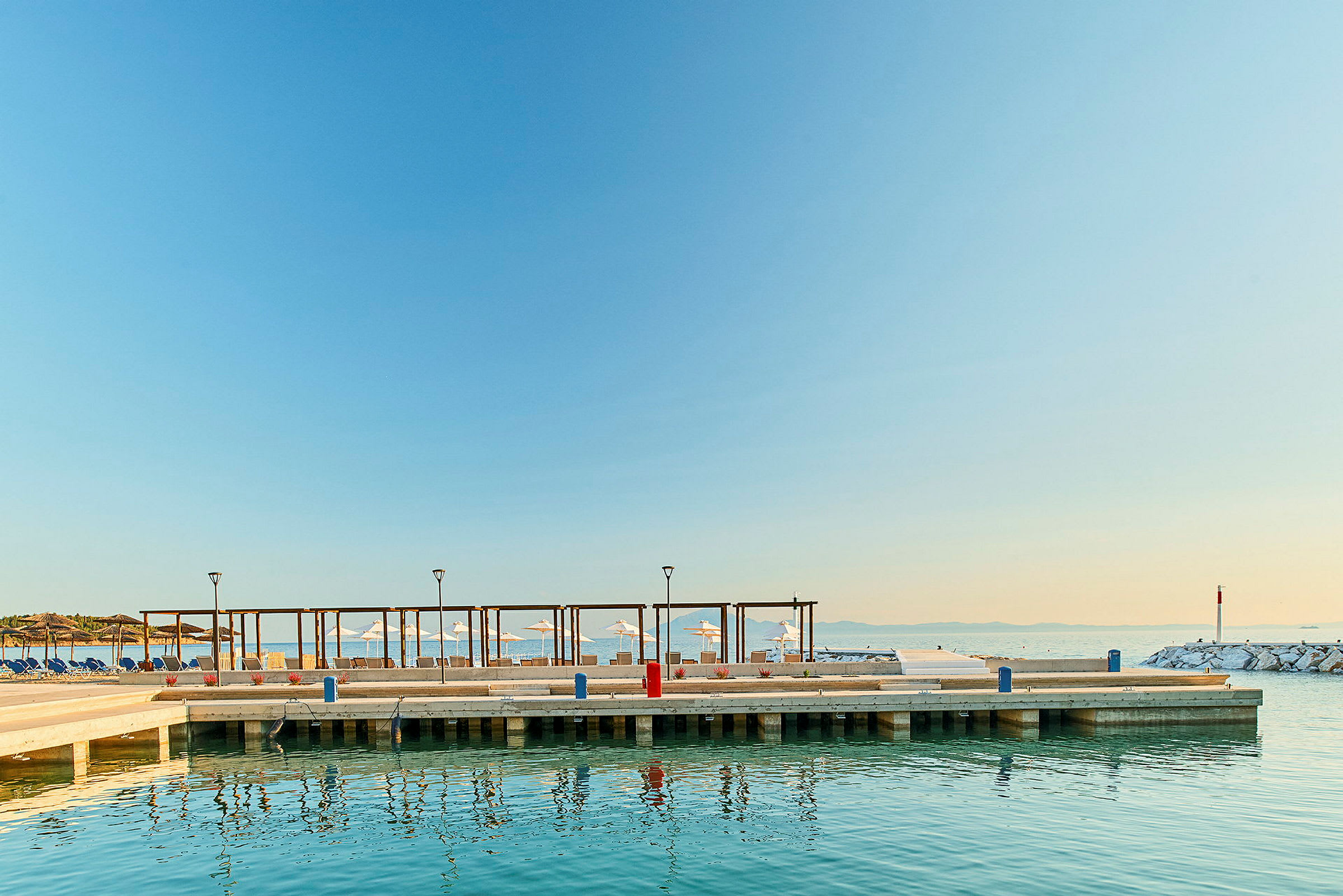 Brygga vid havet med parasoller och solstolar i bakgrunden. (AI-genererad text)