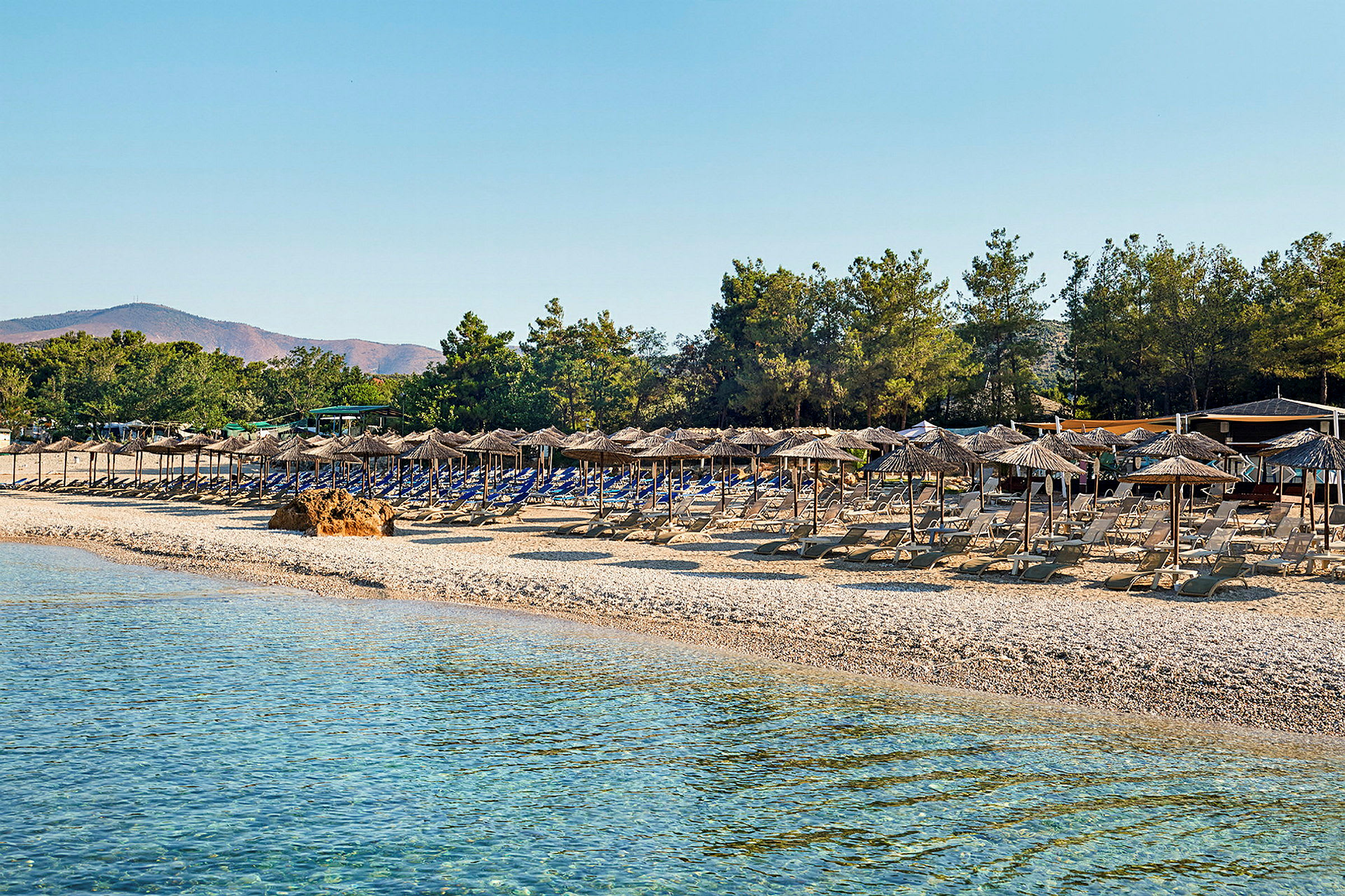 Solstolar och parasoller står uppradade på en strand vid klart vatten. (AI-genererad text)