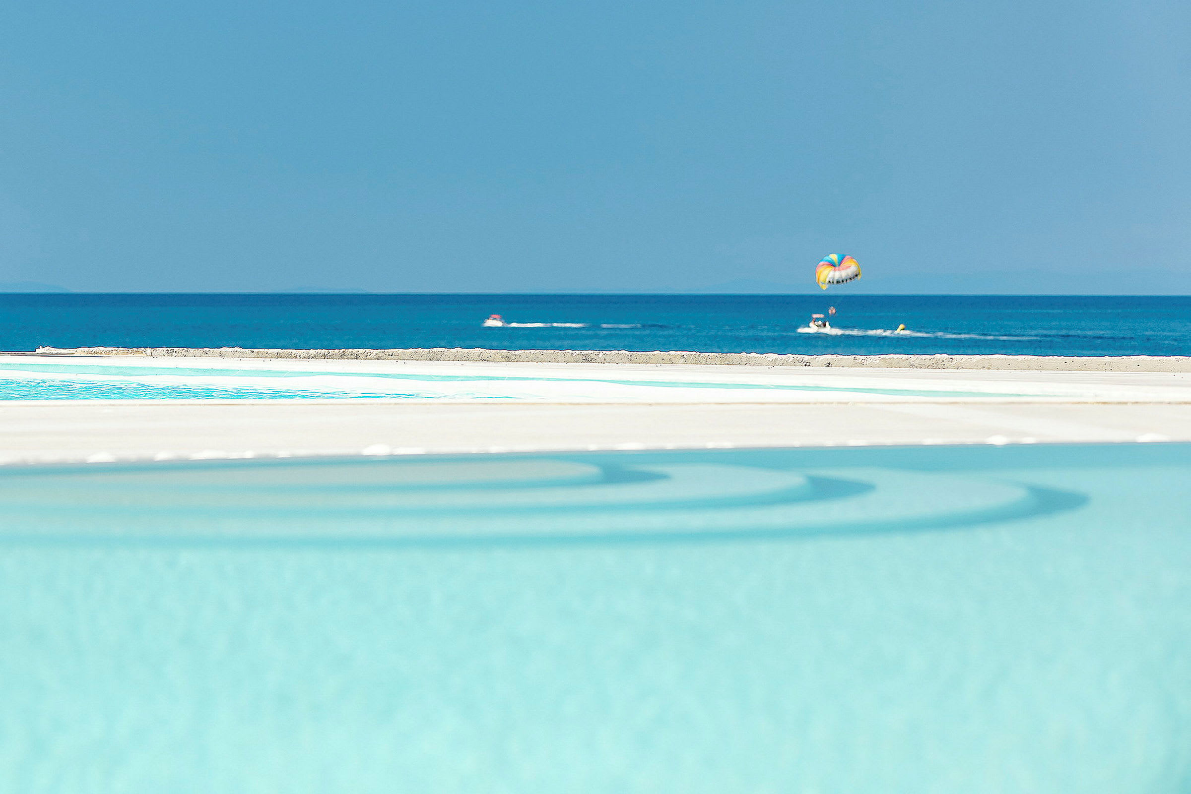 En pool i förgrunden med havet och parasailing i bakgrunden. (AI-genererad text)