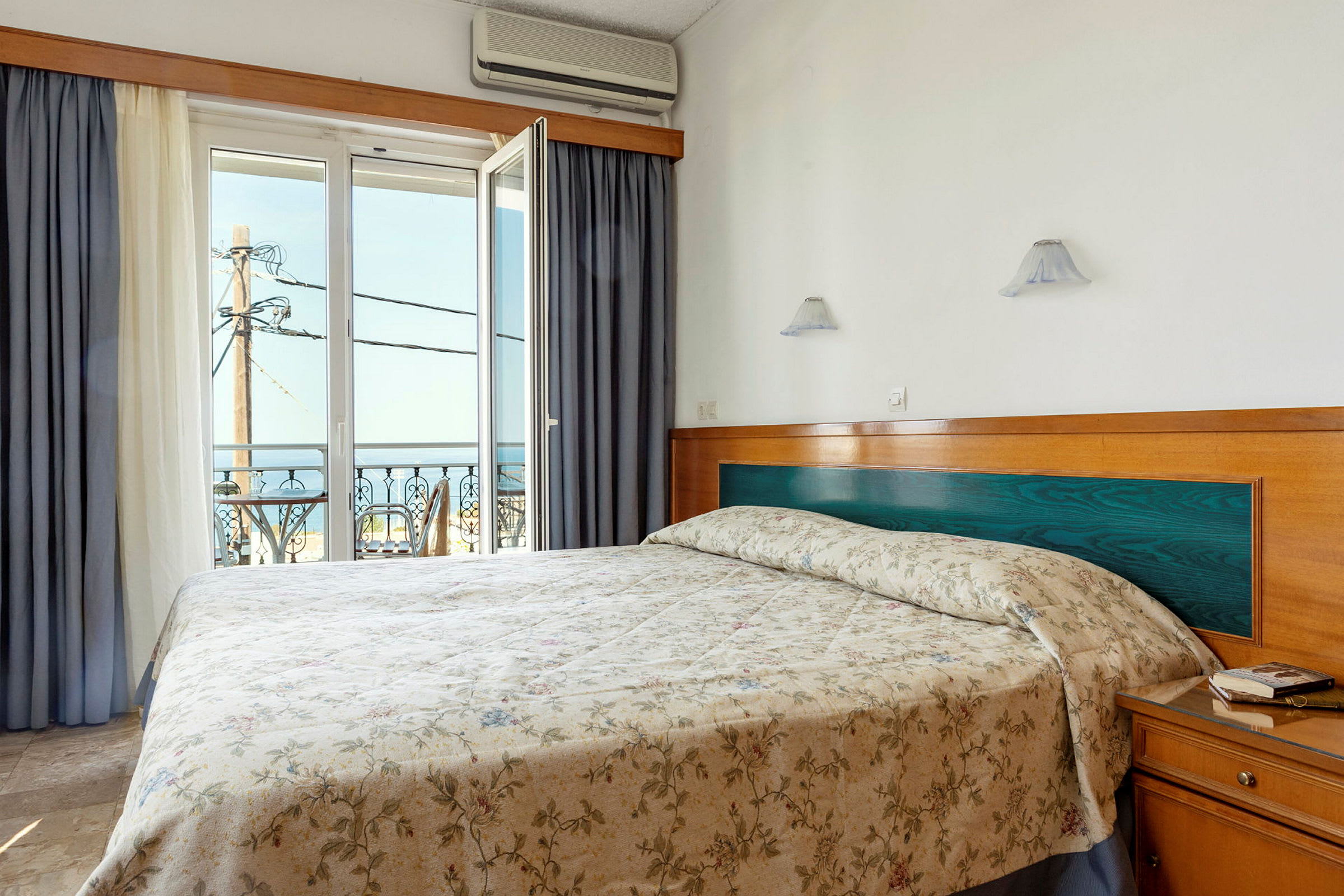 Hotellrum med en dubbelsäng och öppet fönster med utsikt mot havet. (AI-genererad text)
