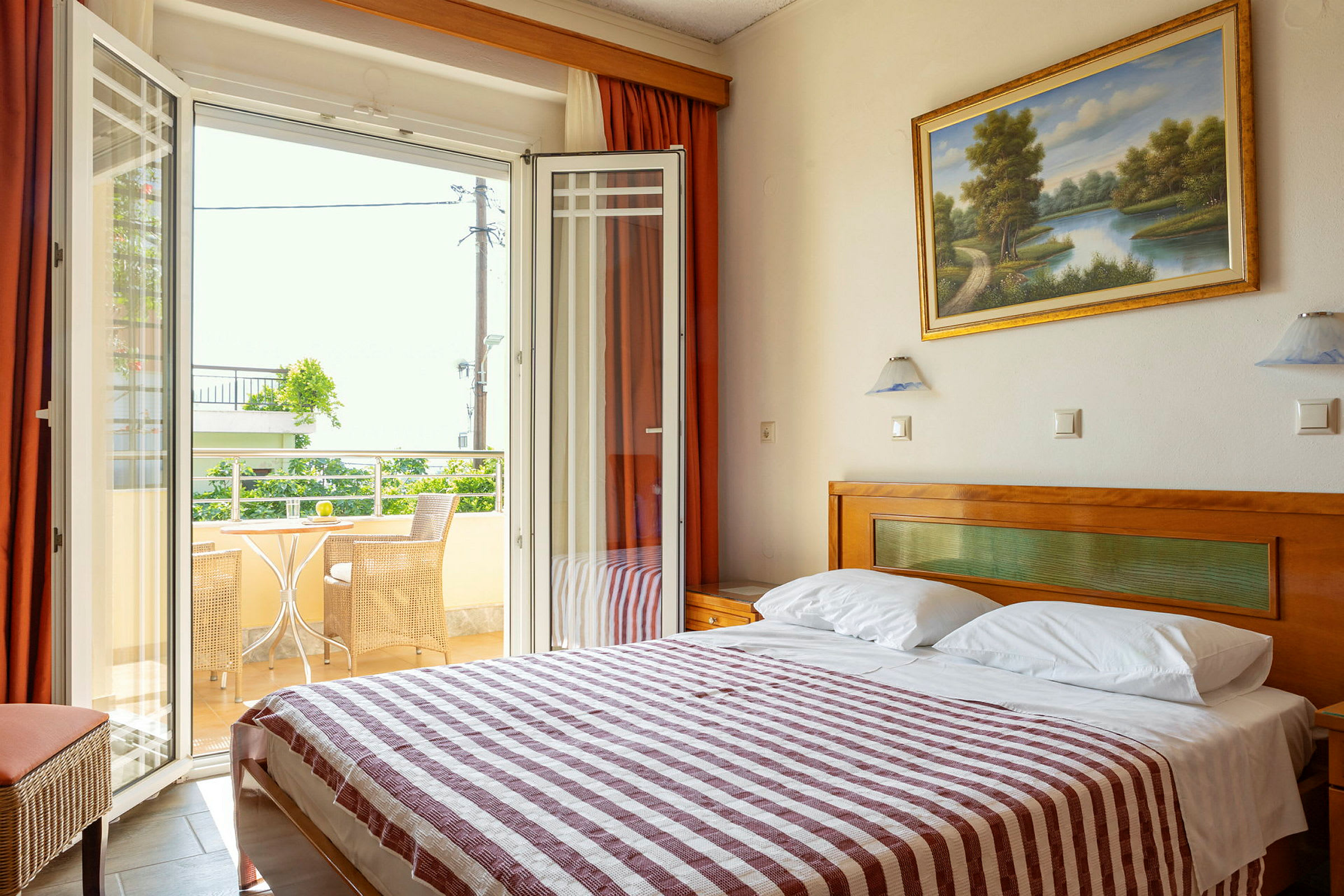 Ett hotellrum med en dubbelsäng och öppna dörrar till en balkong med stolar och bord. (AI-genererad text)