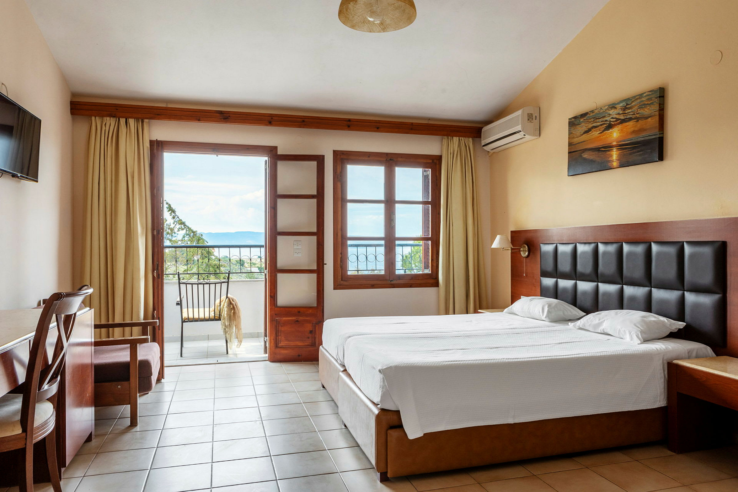 Ett hotellrum med en dubbelsäng, ett skrivbord och en balkong med utsikt. (AI-genererad text)