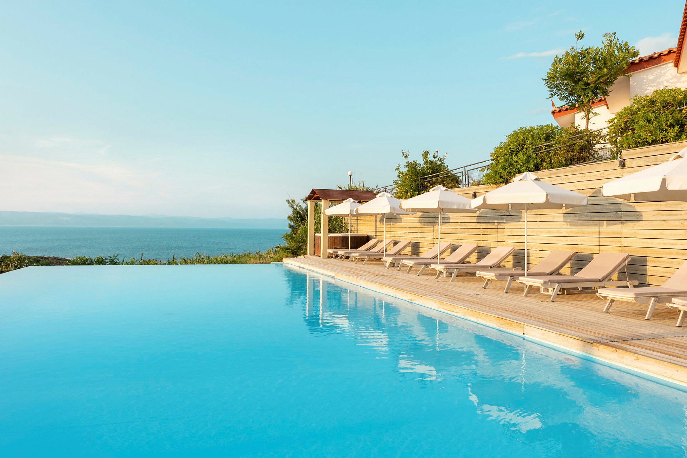 Utsikt över en infinitypool med solstolar och parasoller vid sidan. (AI-genererad text)