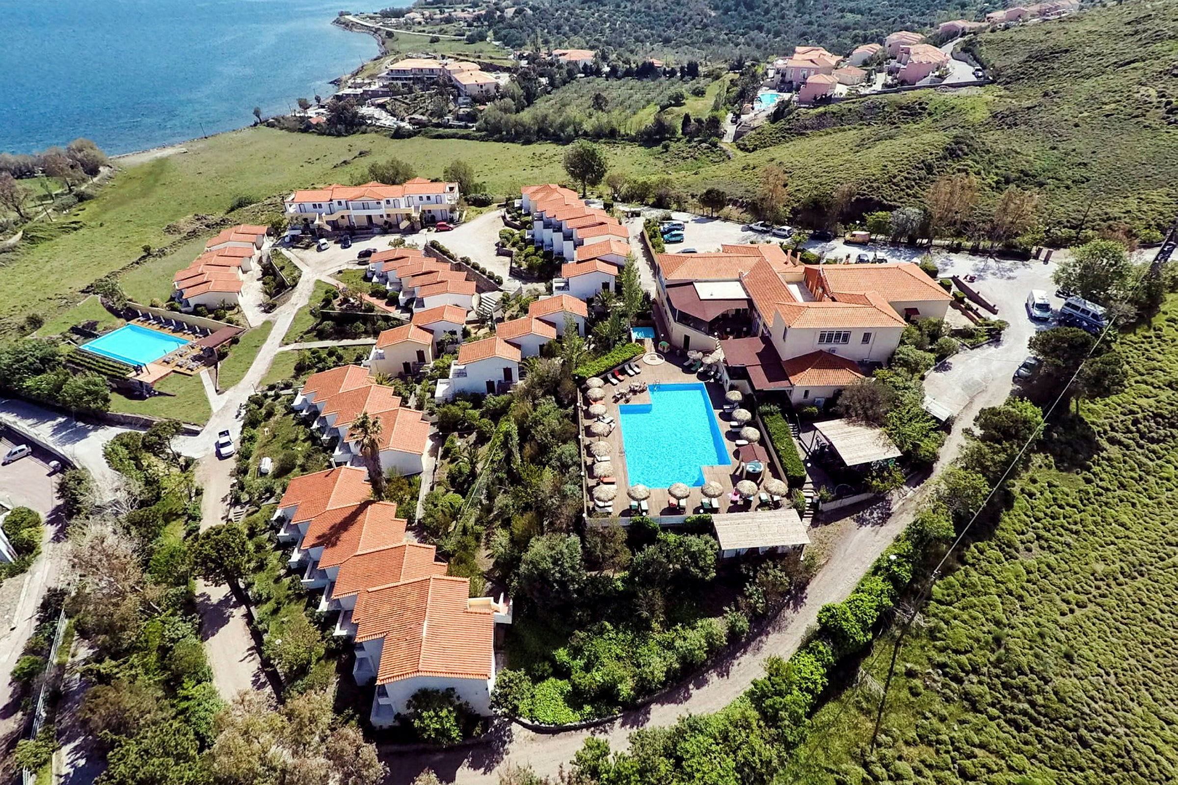 Flygbild över en semesteranläggning vid havet med pool och röda tak. (AI-genererad text)