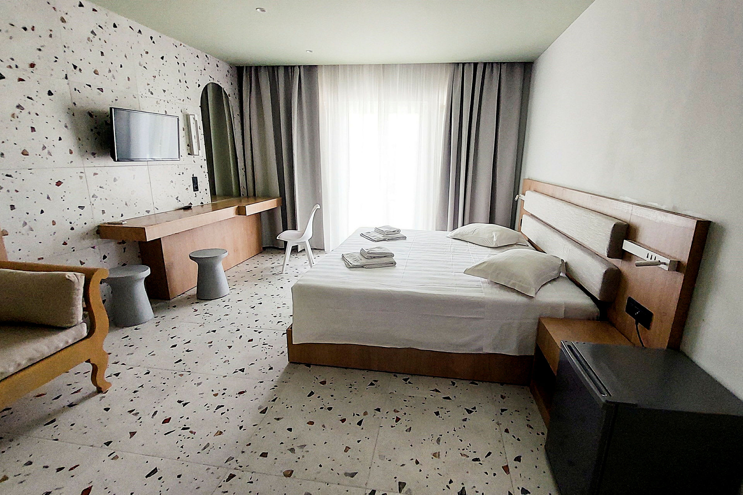 Ett hotellrum med säng, skrivbord och stol, samt ljusa gardiner vid fönstret. (AI-genererad text)
