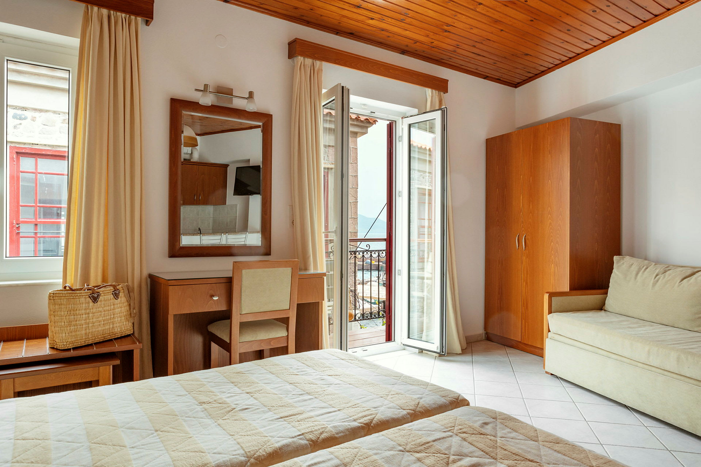 Ett hotellrum med två sängar, en spegel över ett skrivbord och en stol, samt en öppen balkongdörr med utsikt. (AI-genererad text)