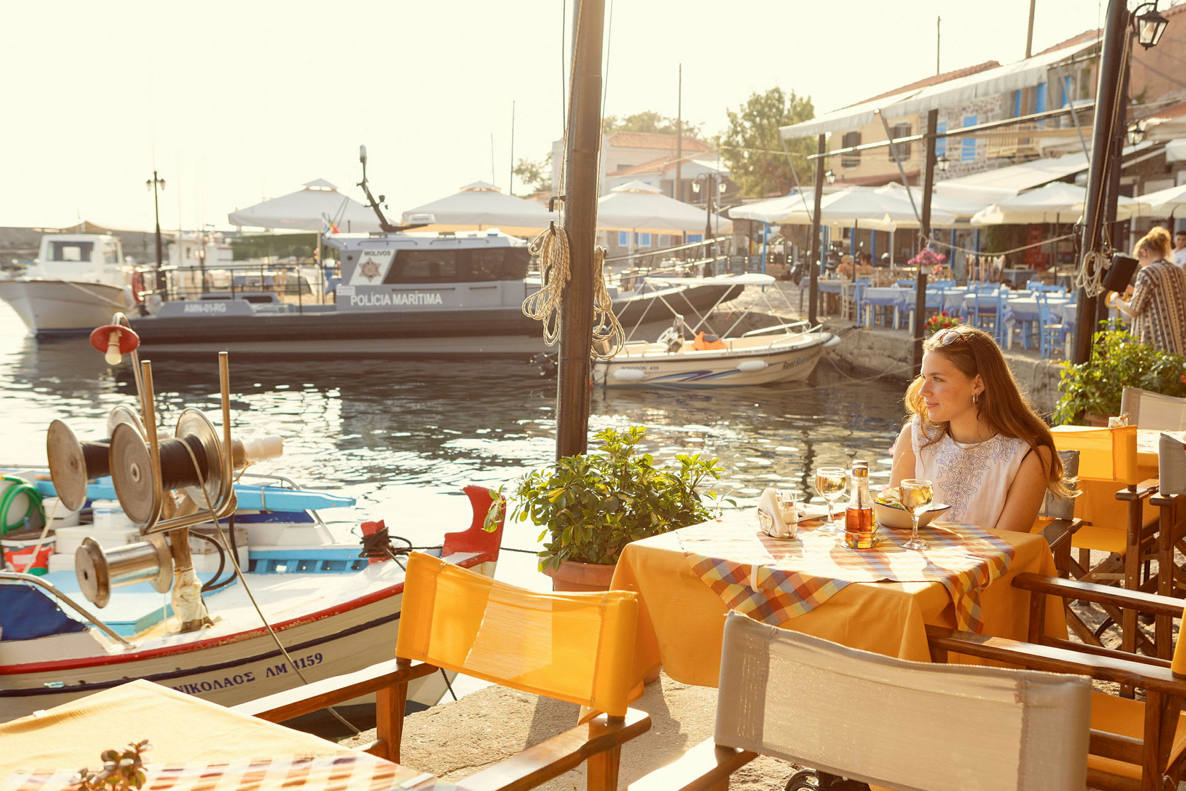 En utomhus restaurang med utsikt över en marina med småbåtar och en polisbåt. (AI-genererad text)