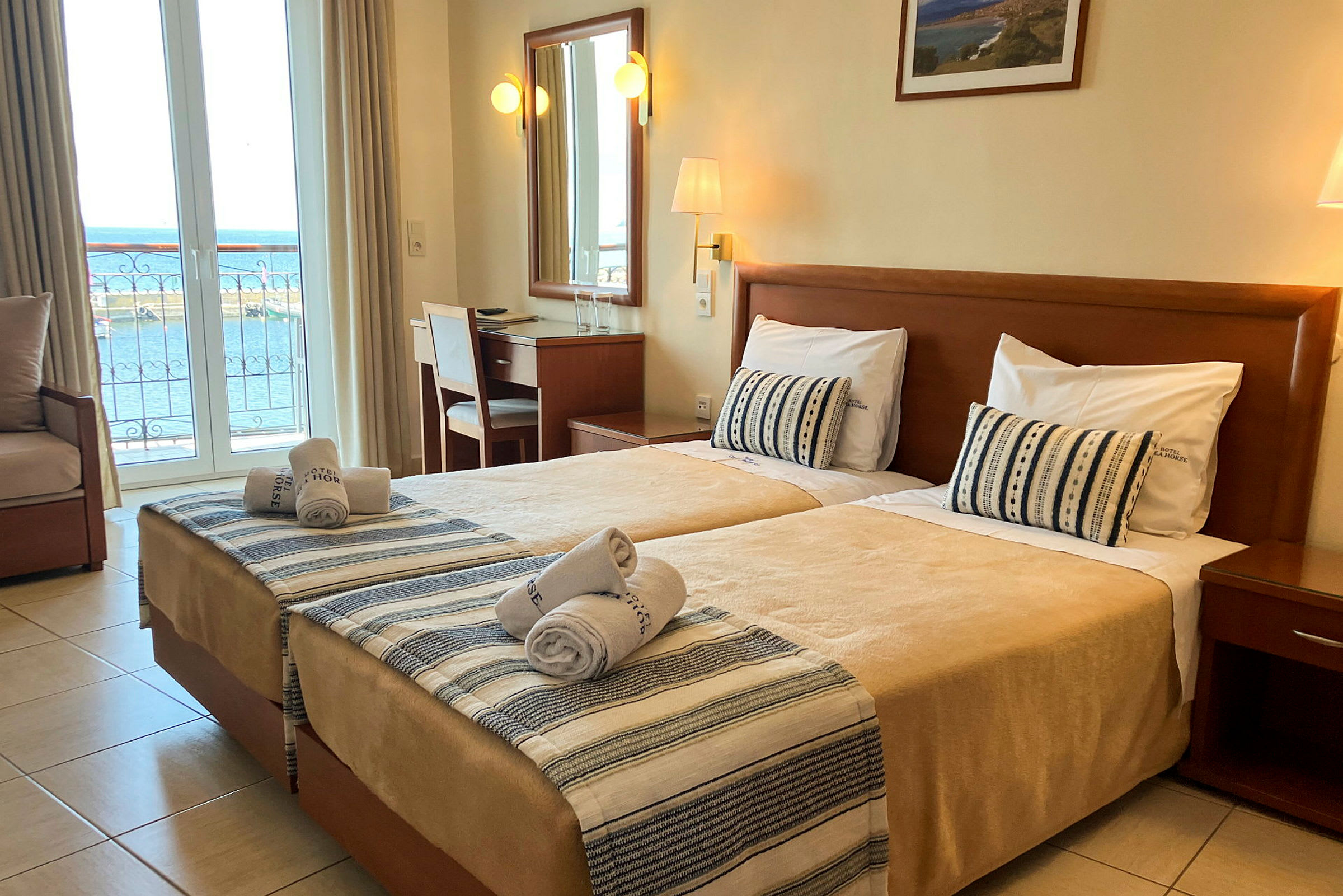 Hotellrum med två enkelsängar, skrivbord och utsikt över havet från balkongen. (AI-genererad text)