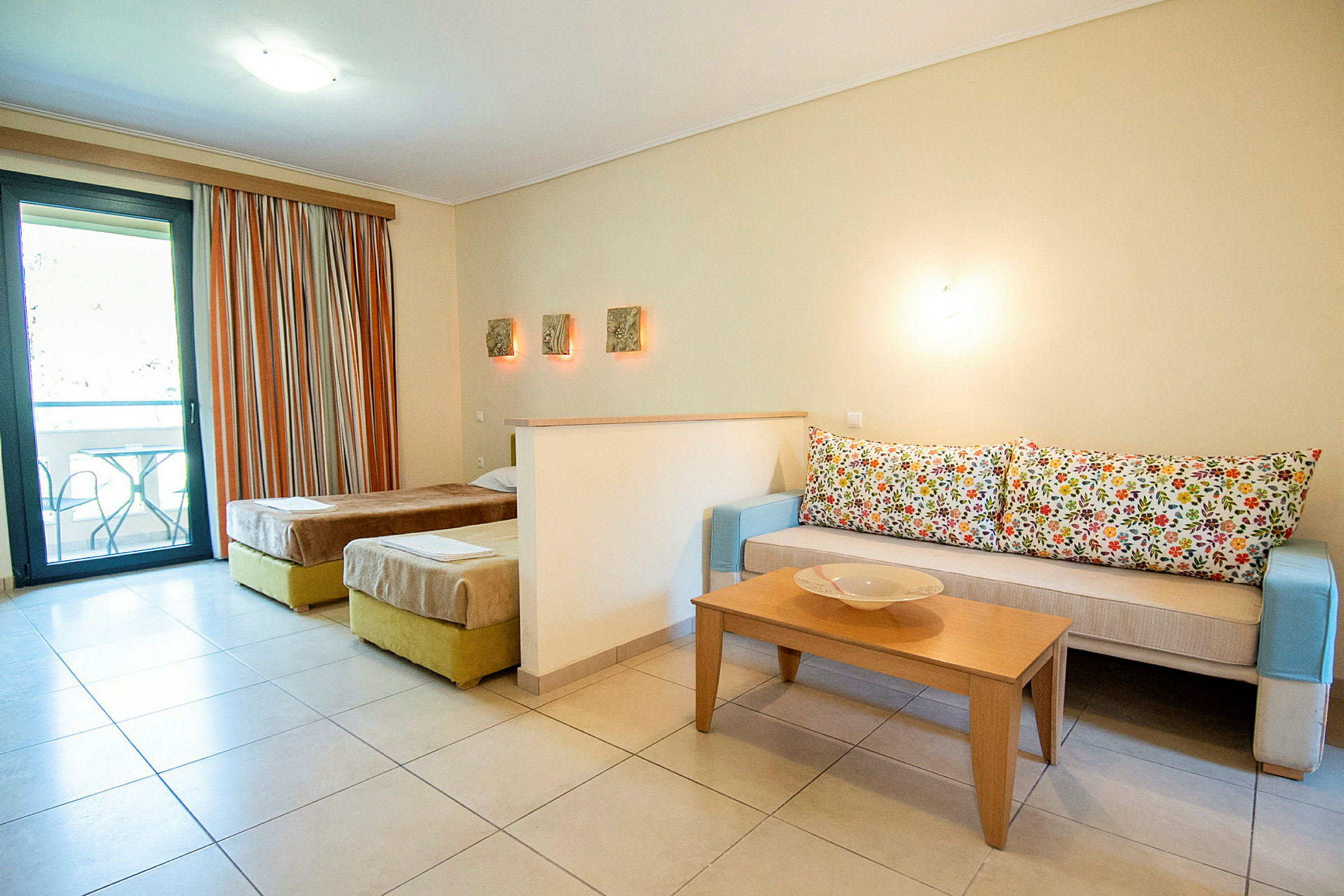 Ett hotellrum med två enkelsängar, en soffa med mönstrade kuddar och ett soffbord. (AI-genererad text)