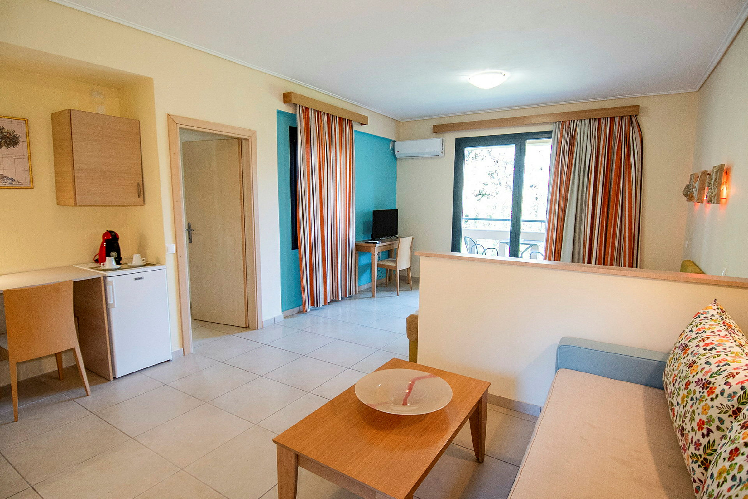 En hotellrumsinteriör med sittgrupp, köksdel och balkongdörr. (AI-genererad text)