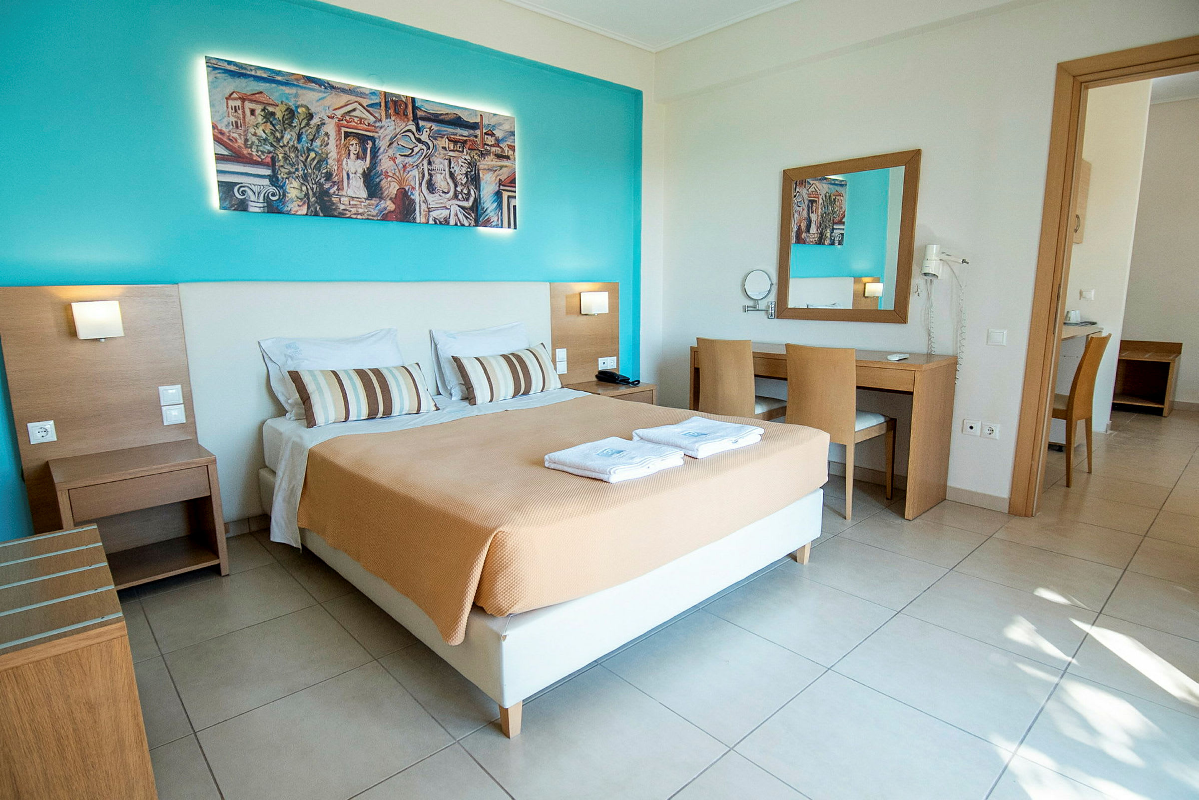 Ett hotellrum med en dubbelsäng, skrivbord och stol, samt väggdekorationer och spegel. (AI-genererad text)