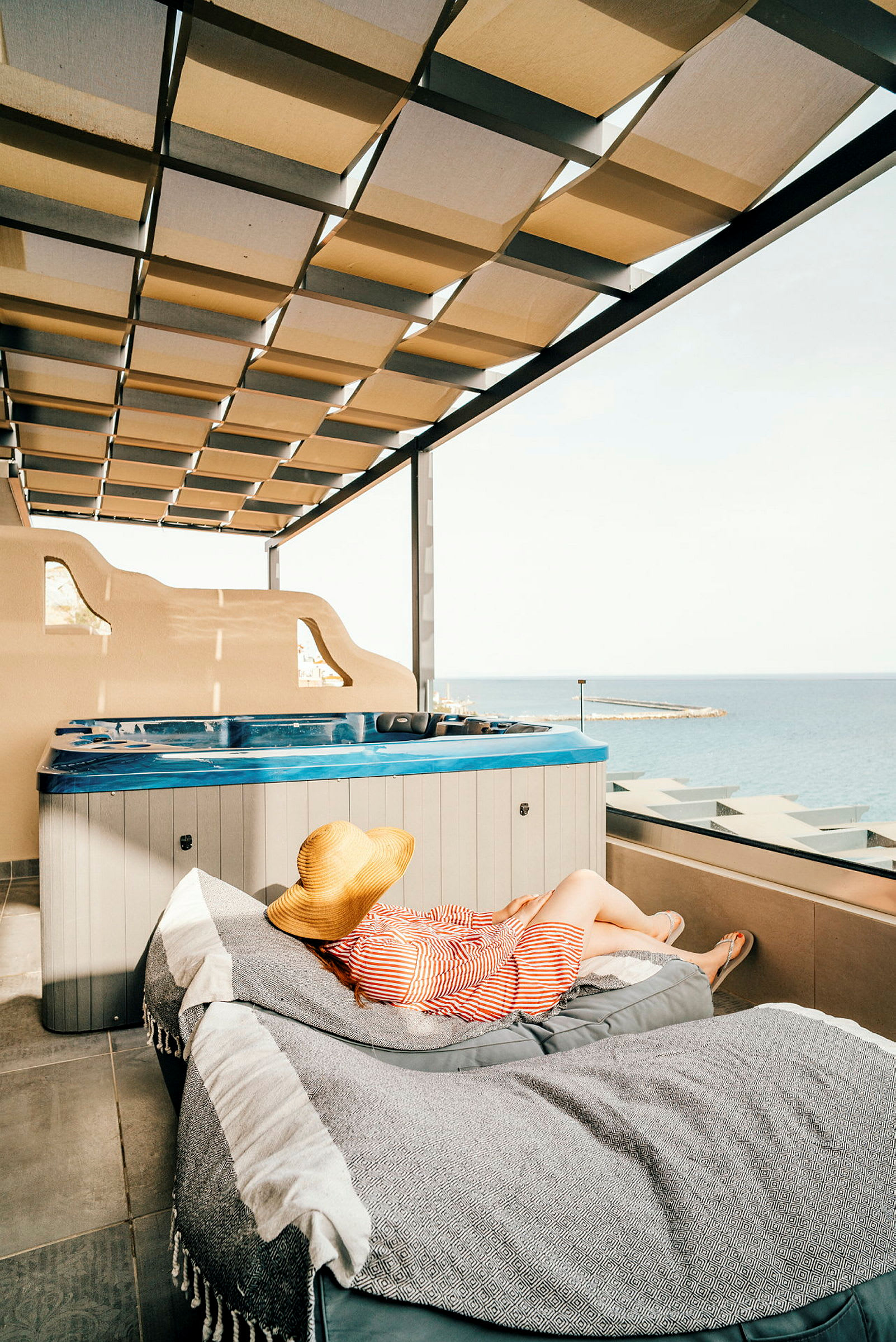 Person ligger i solstol bredvid en jacuzzi med utsikt över havet. (AI-genererad text)