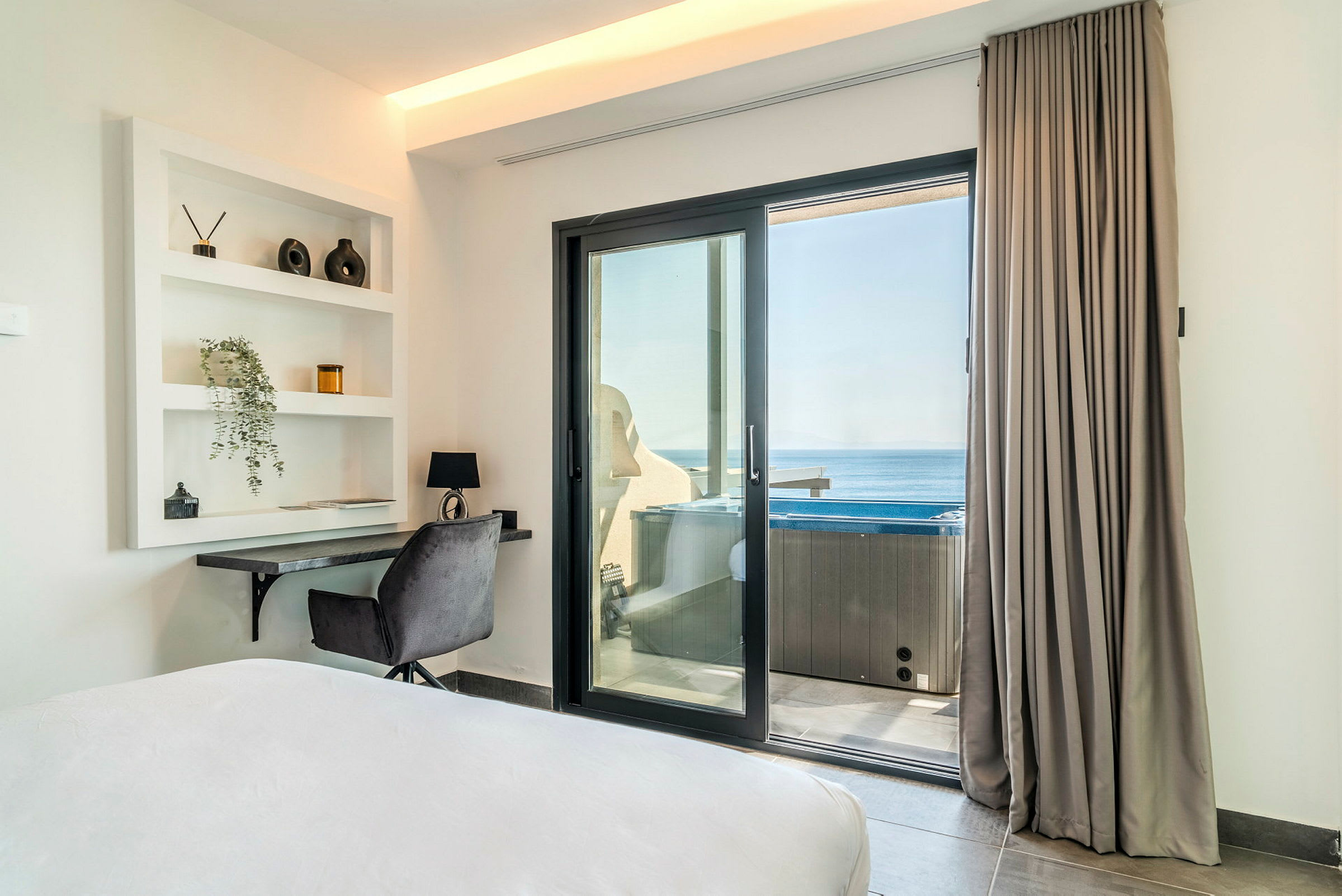 Ett hotellrum med en arbetsplats och en skjutdörr som leder till en balkong med utsikt över havet. (AI-genererad text)