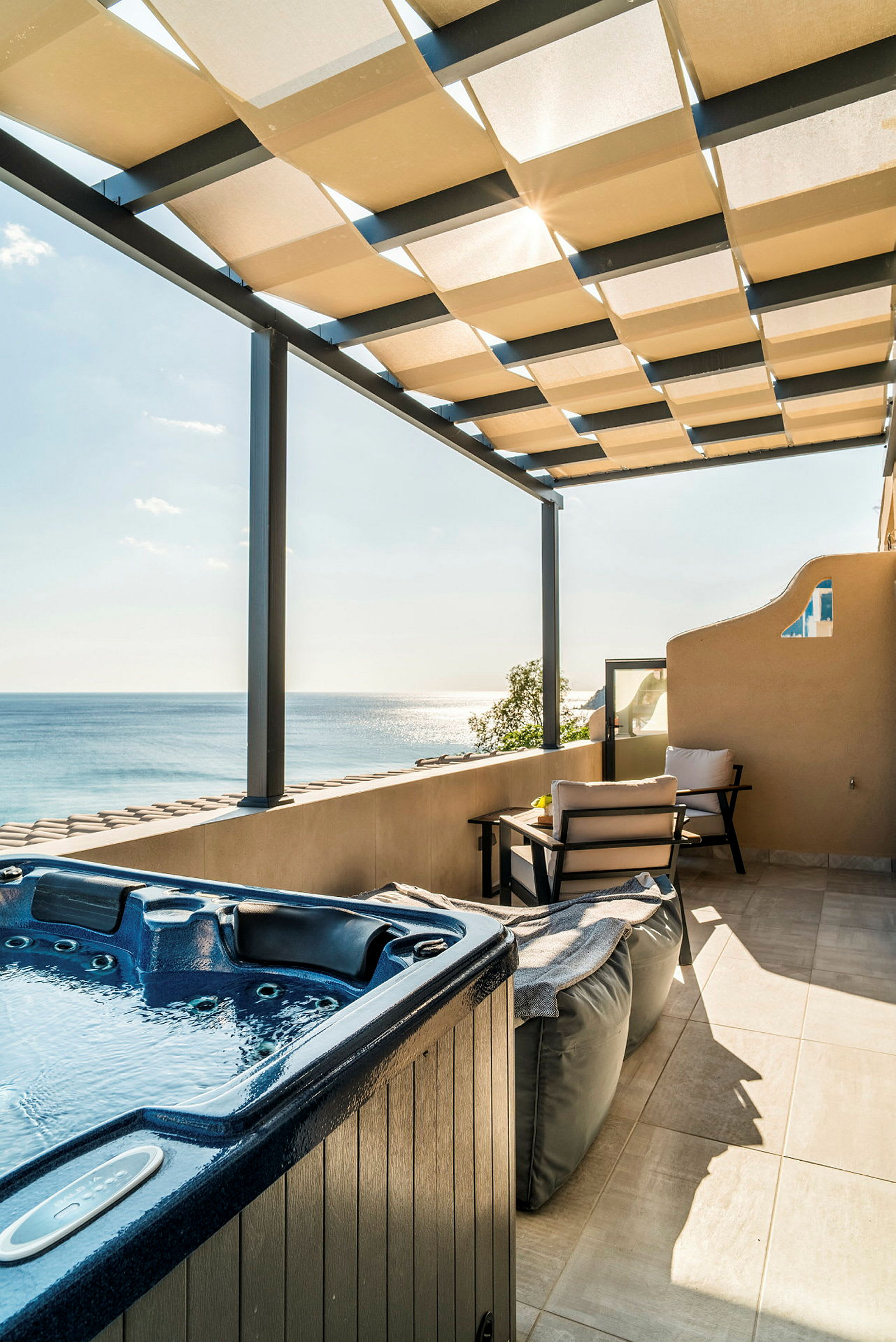 En terrass med en jacuzzi, sittmöbler och utsikt över havet under en takpergola. (AI-genererad text)