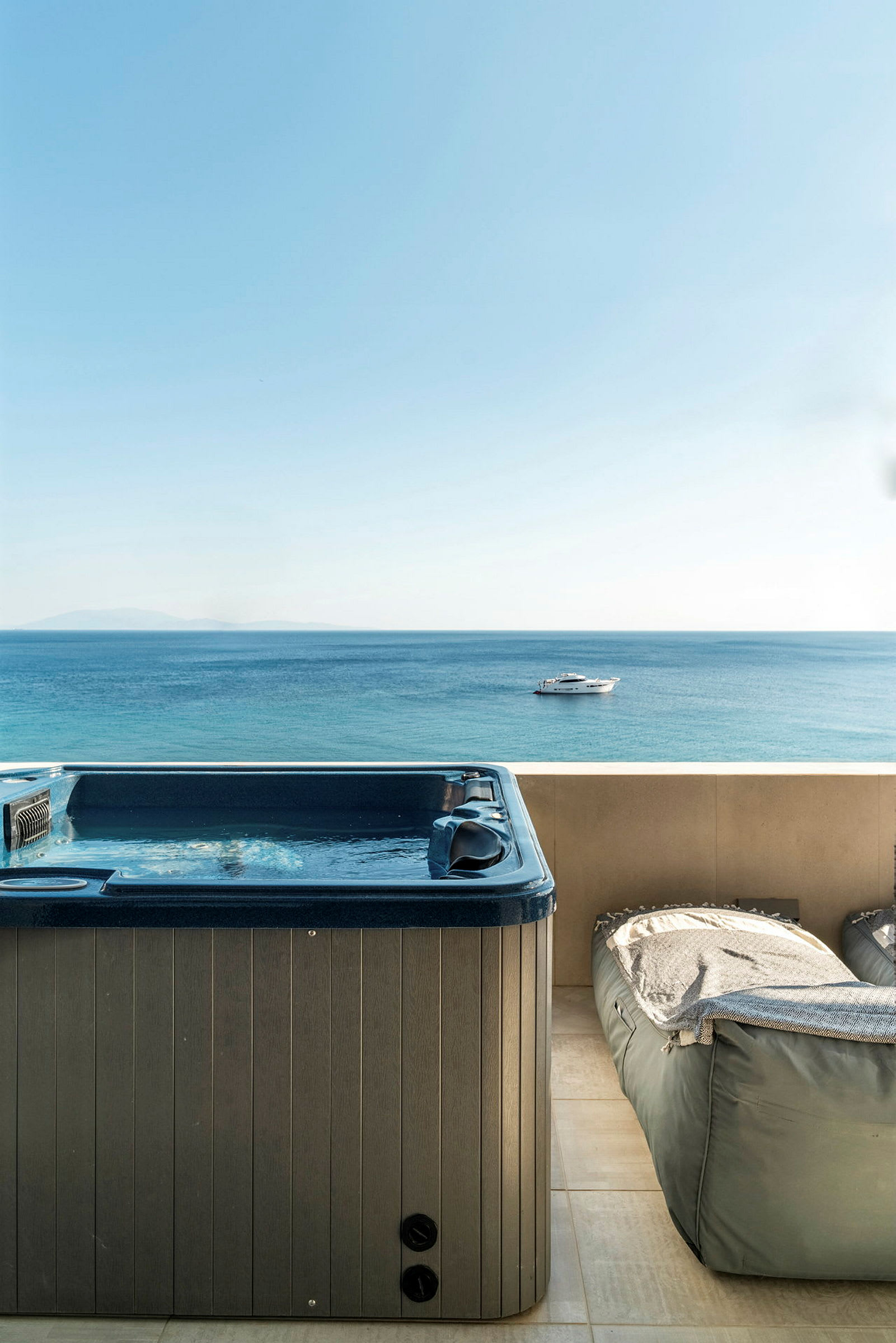 Utomhusjacuzzi vid en terrass med utsikt över havet och en båt. (AI-genererad text)