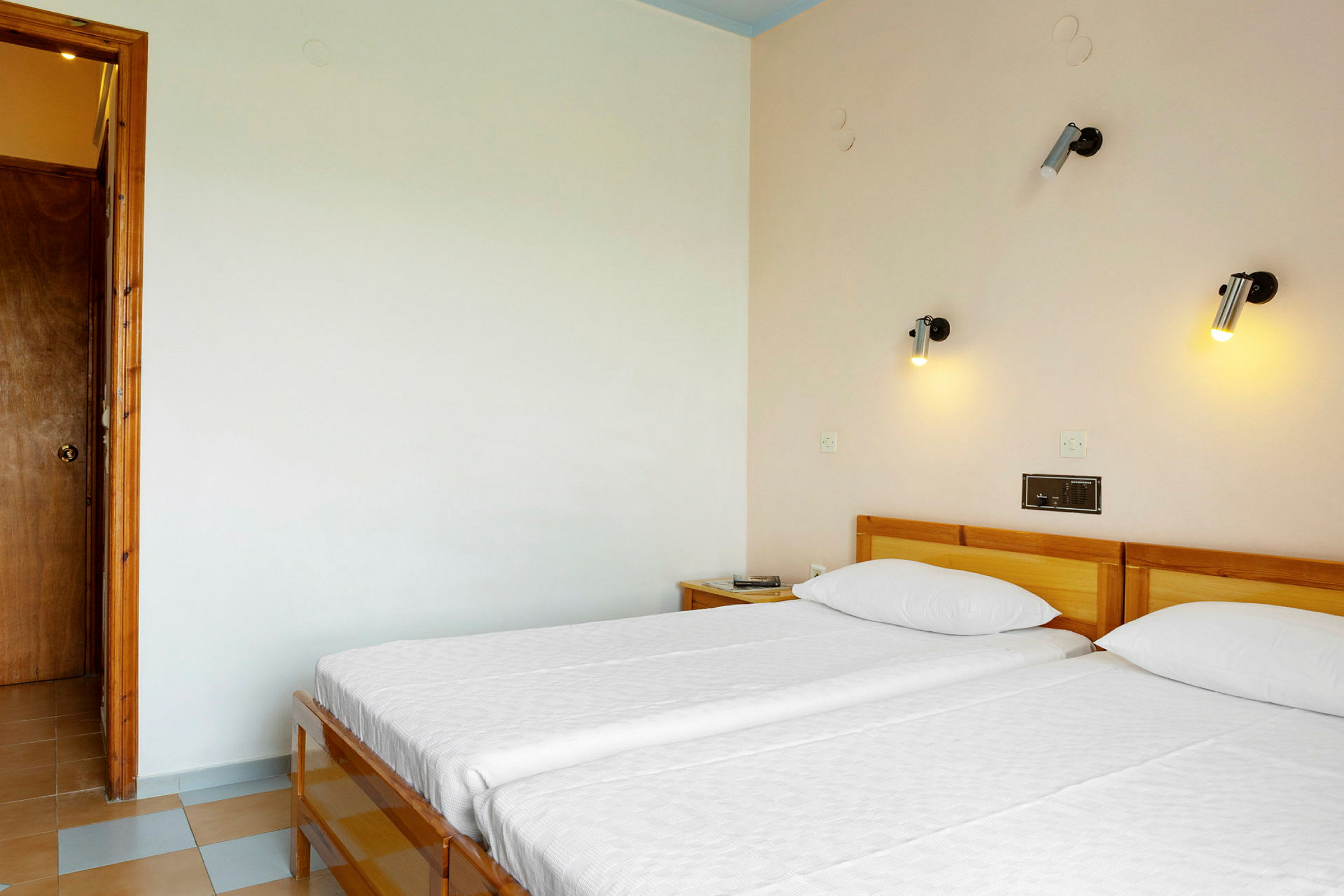 Hotellrum med två enkelsängar och vägglampor ovanför sängarna. (AI-genererad text)