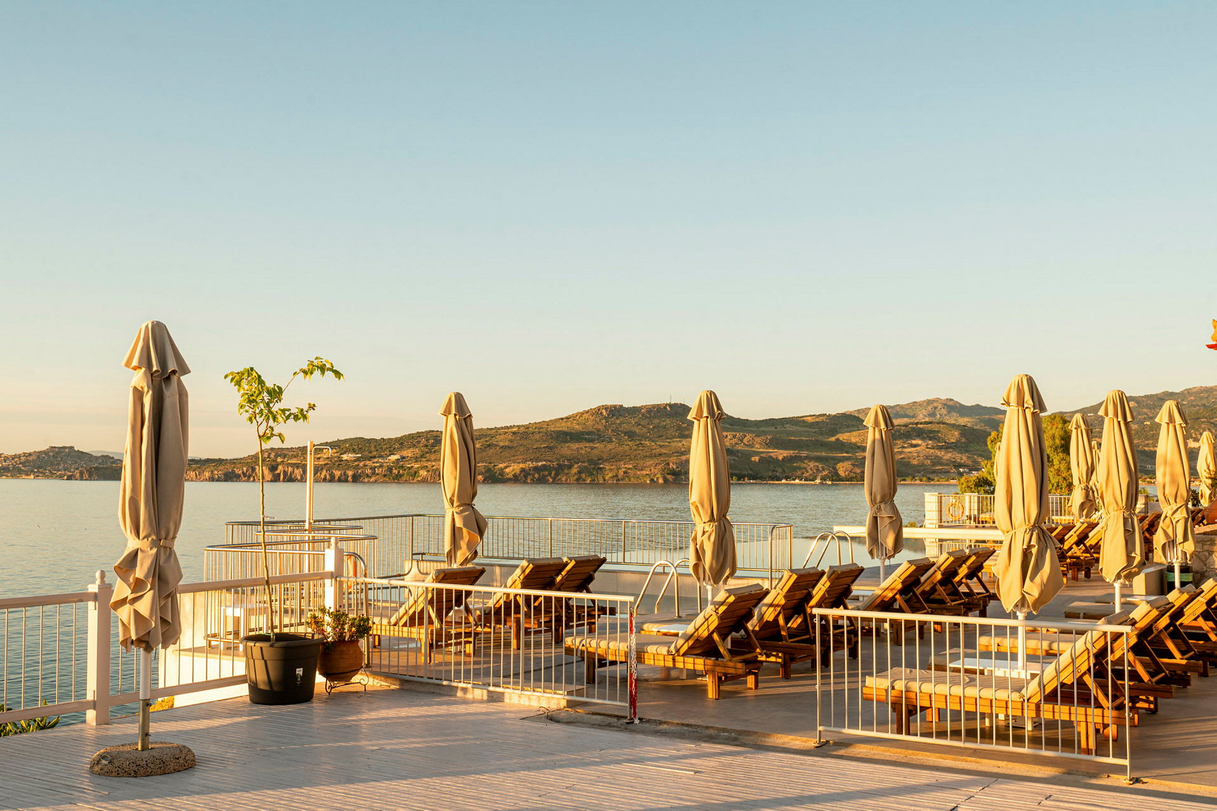 En solterrass med solstolar och parasoller med utsikt över havet och berg i bakgrunden. (AI-genererad text)