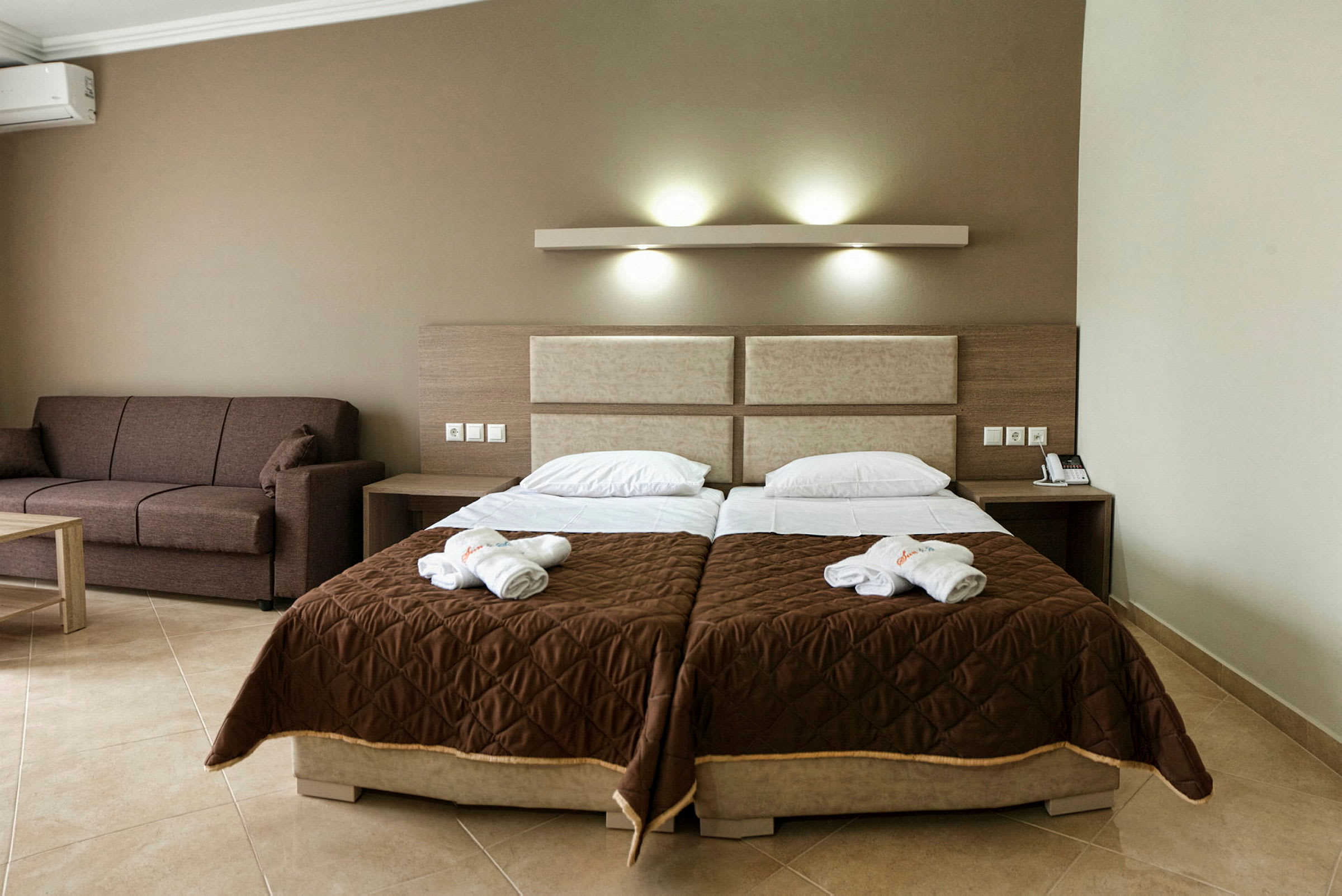 Hotellrum med två enkelsängar och en brun soffa. (AI-genererad text)
