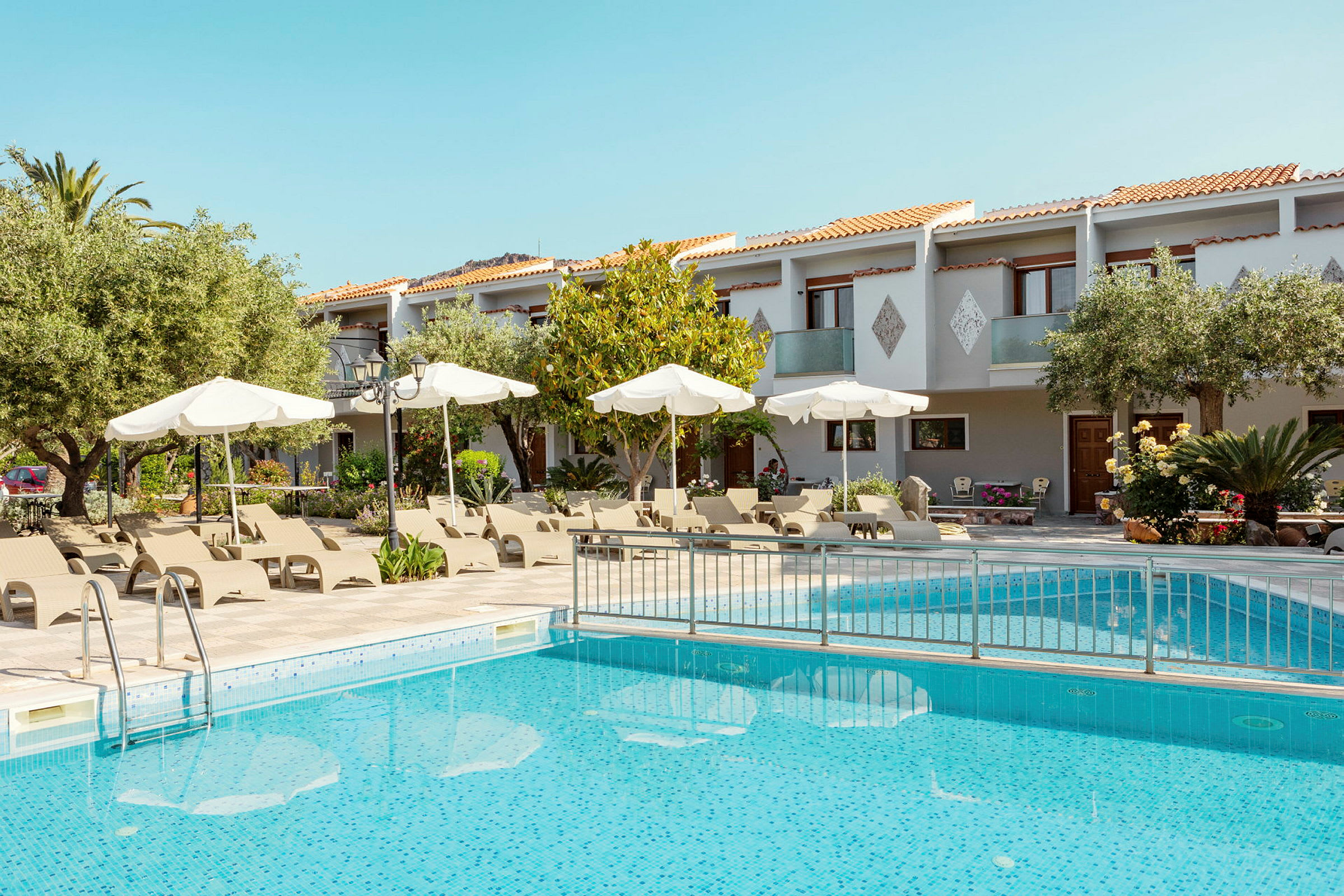 En pool med solstolar och parasoller framför en byggnad med balkonger. (AI-genererad text)