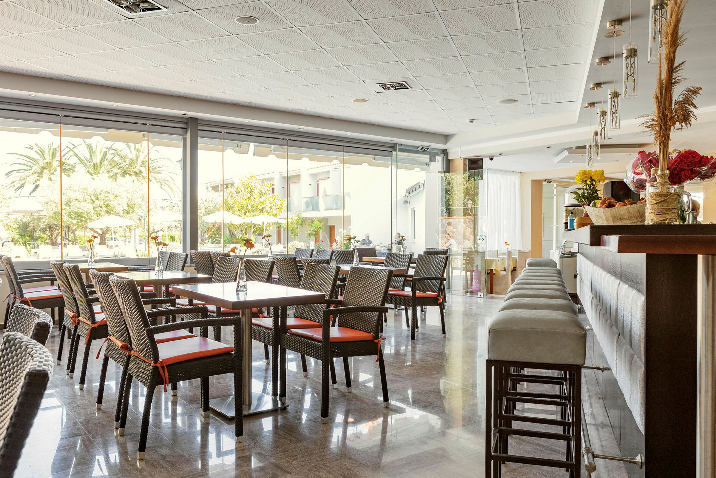 En hotellrestaurang med bord och stolar samt en bardisk, stora fönster mot utomhus. (AI-genererad text)