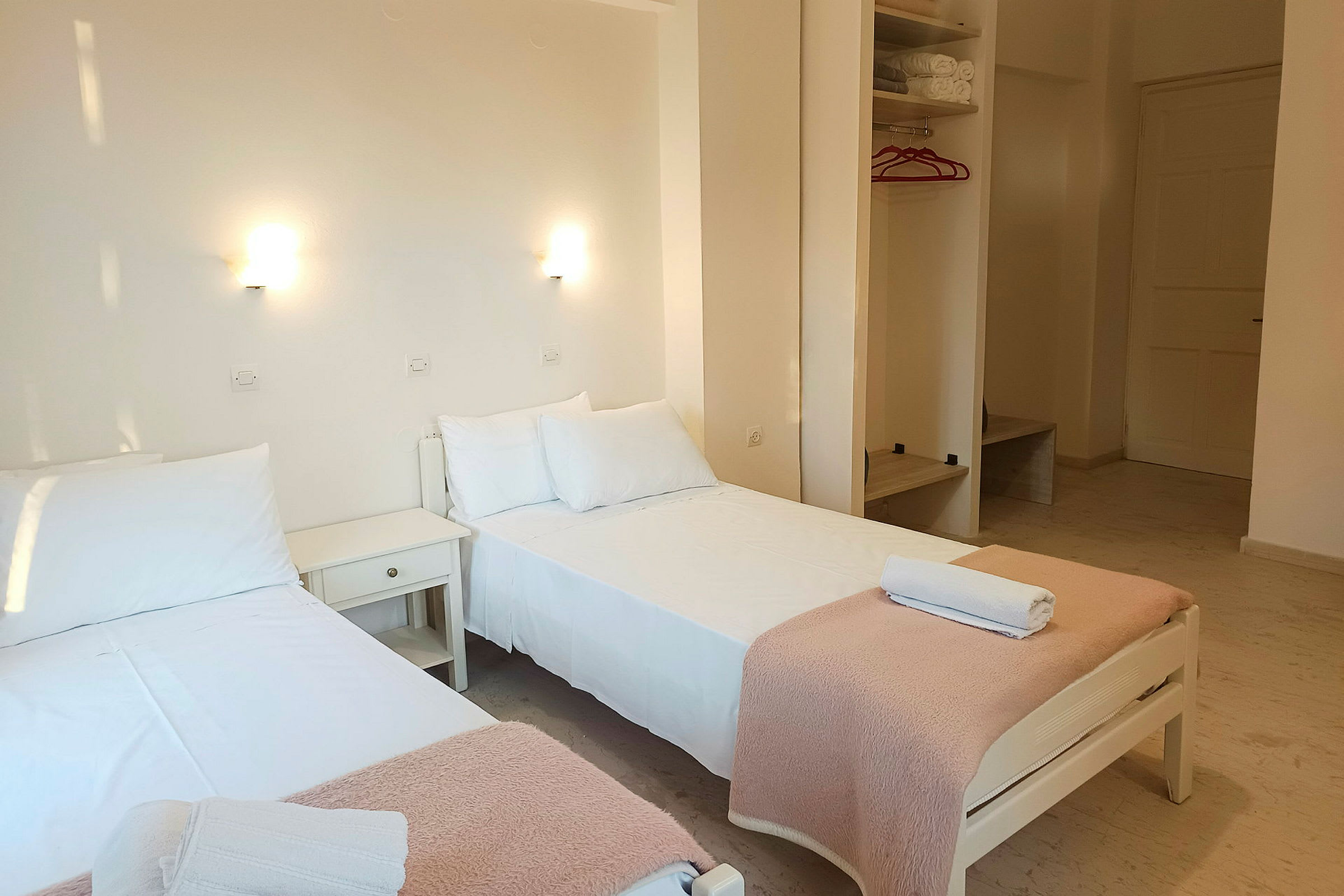Två enkelsängar med vita lakan och rosa filtar står i ett ljust rum. (AI-genererad text)