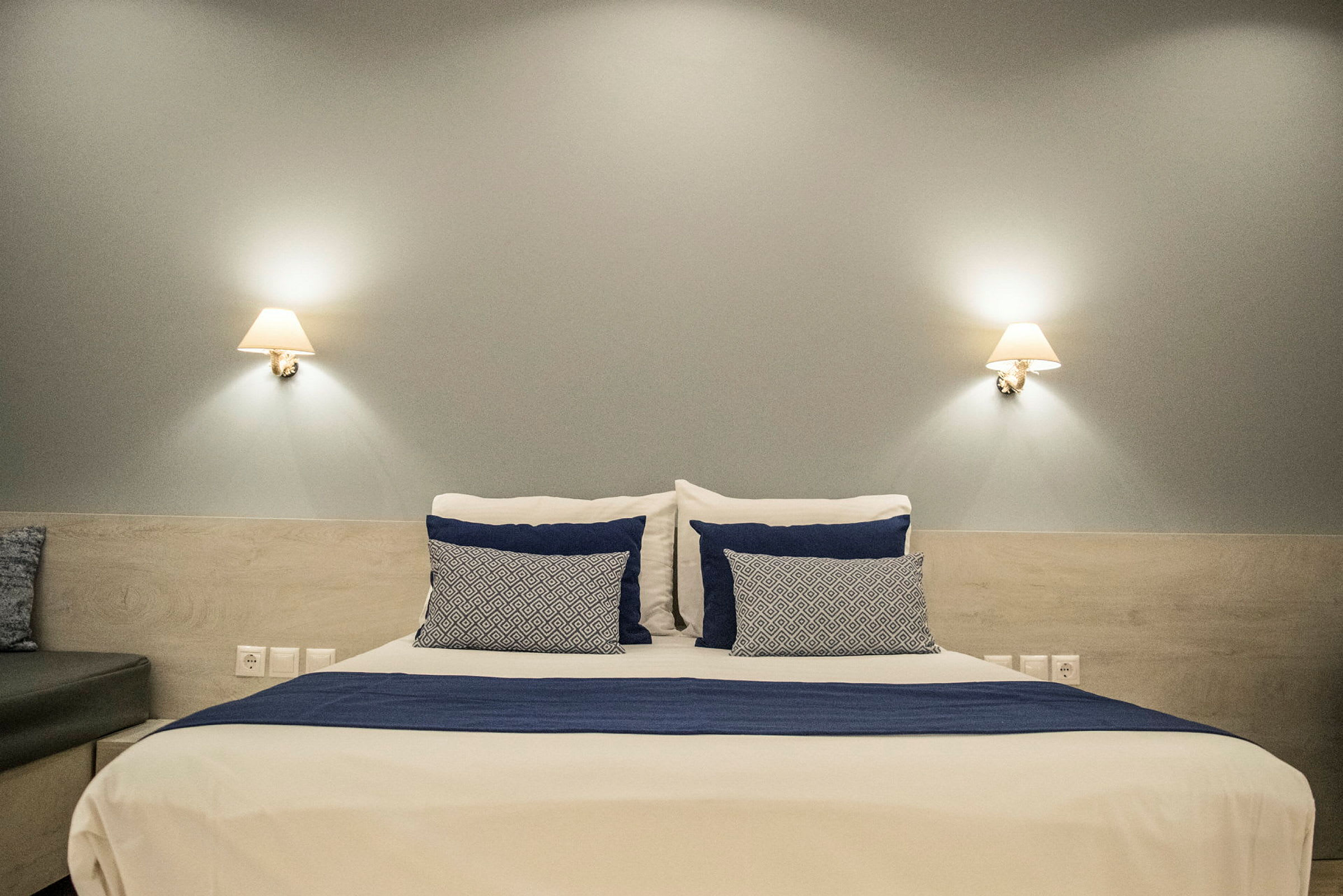 Bild av en säng med vita och blå sängkläder, flankerad av två vägglampor. (AI-genererad text)