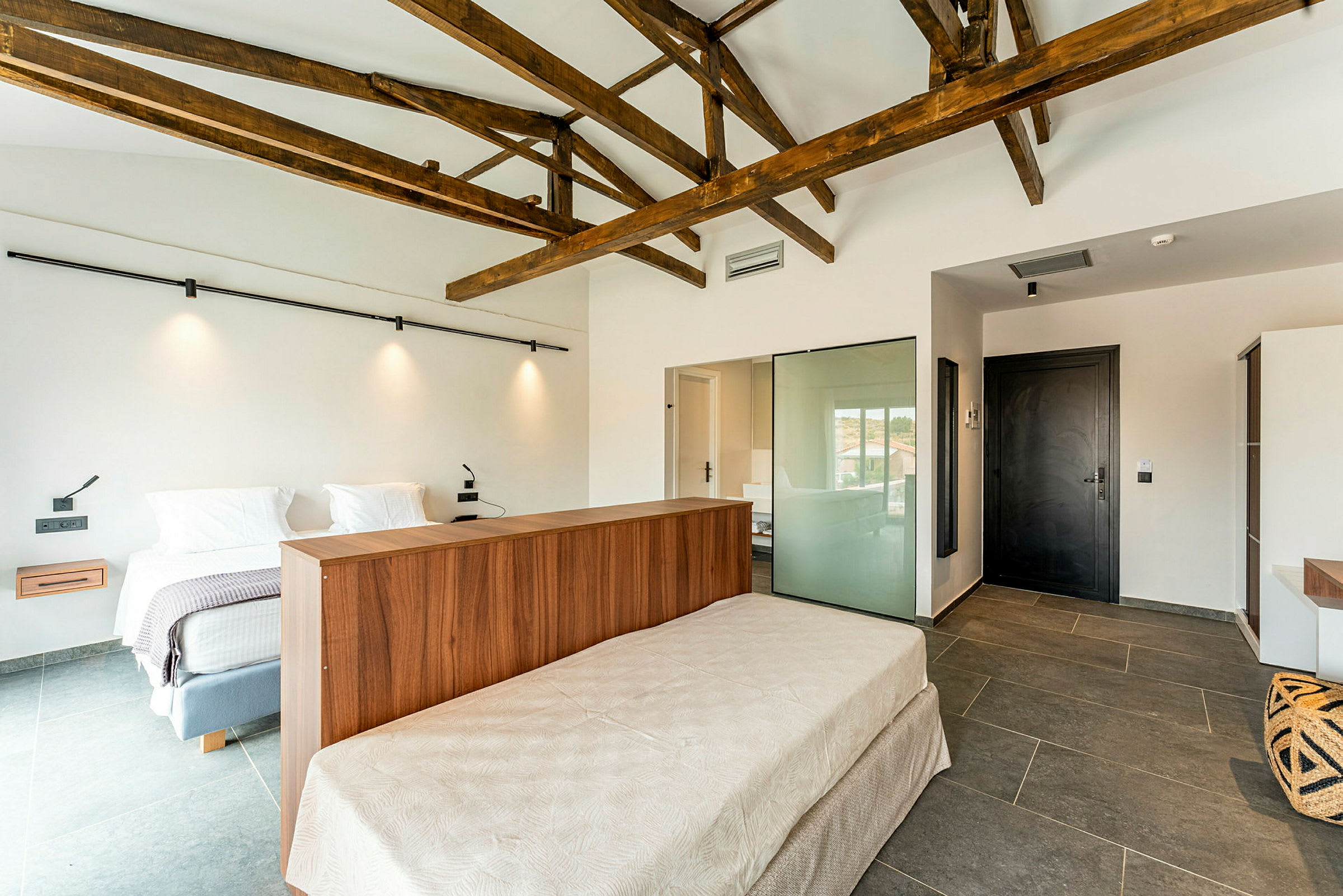 Ett hotellrum med modern inredning, sängar, träbjälkar i taket och stengolv. (AI-genererad text)