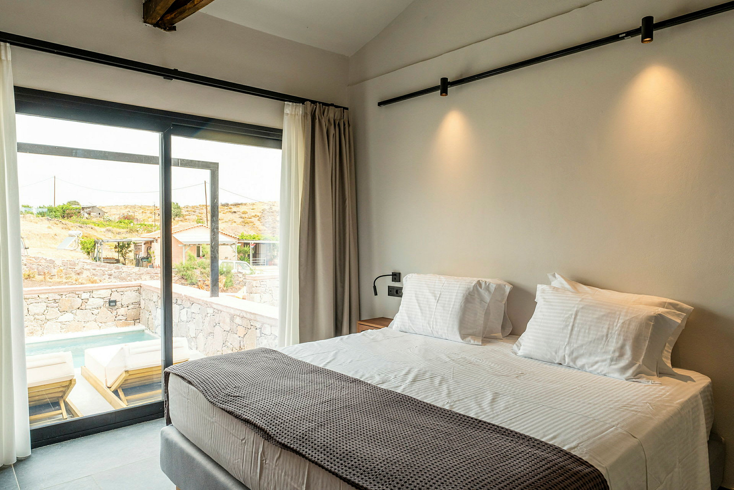 Hotellrum med stor säng vid ett fönster som vetter mot en uteplats med solsängar och liten pool. (AI-genererad text)