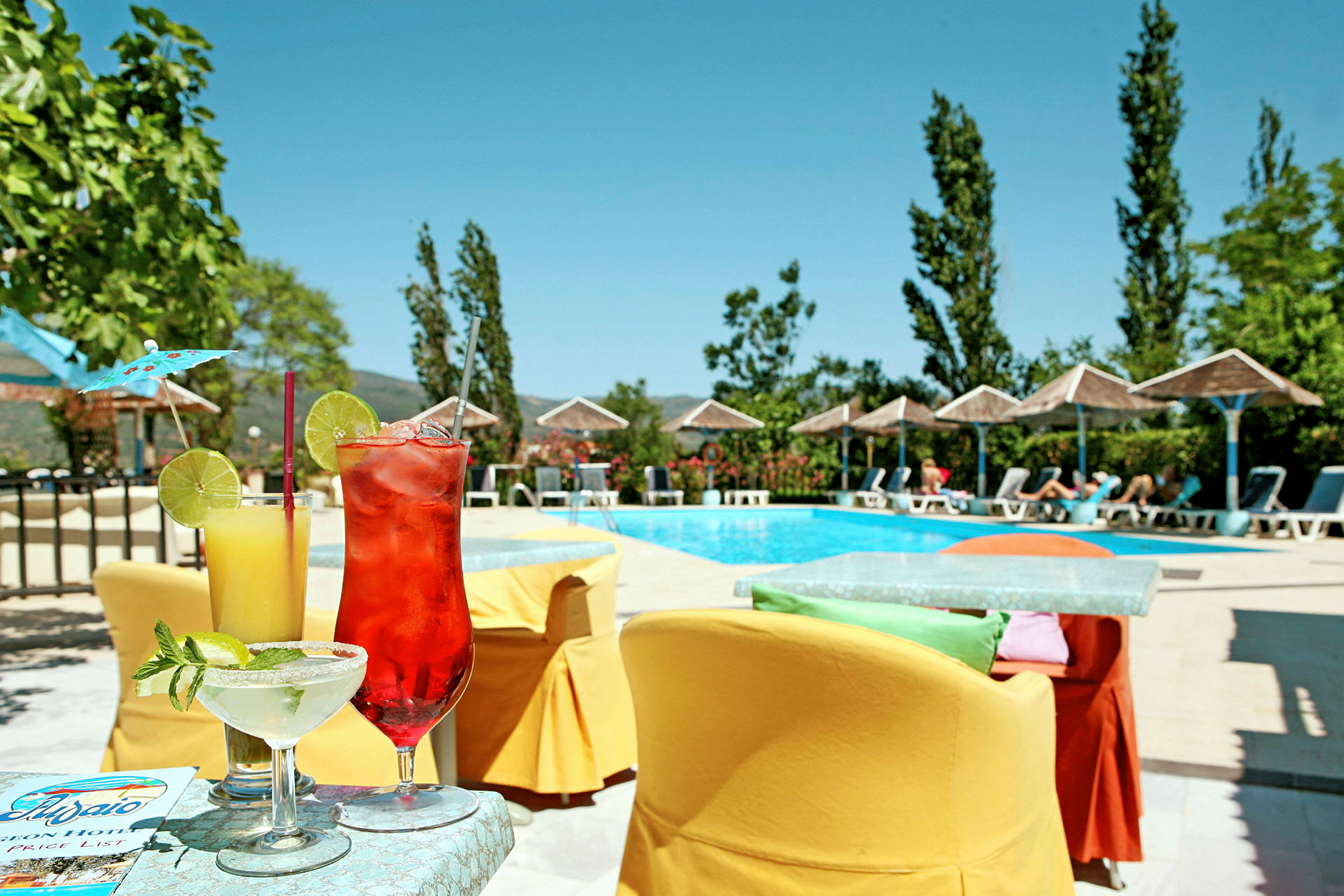 Bild av en pool omgiven av solstolar och parasoller. På ett bord i förgrunden står tre färgglada drinkar. (AI-genererad text)