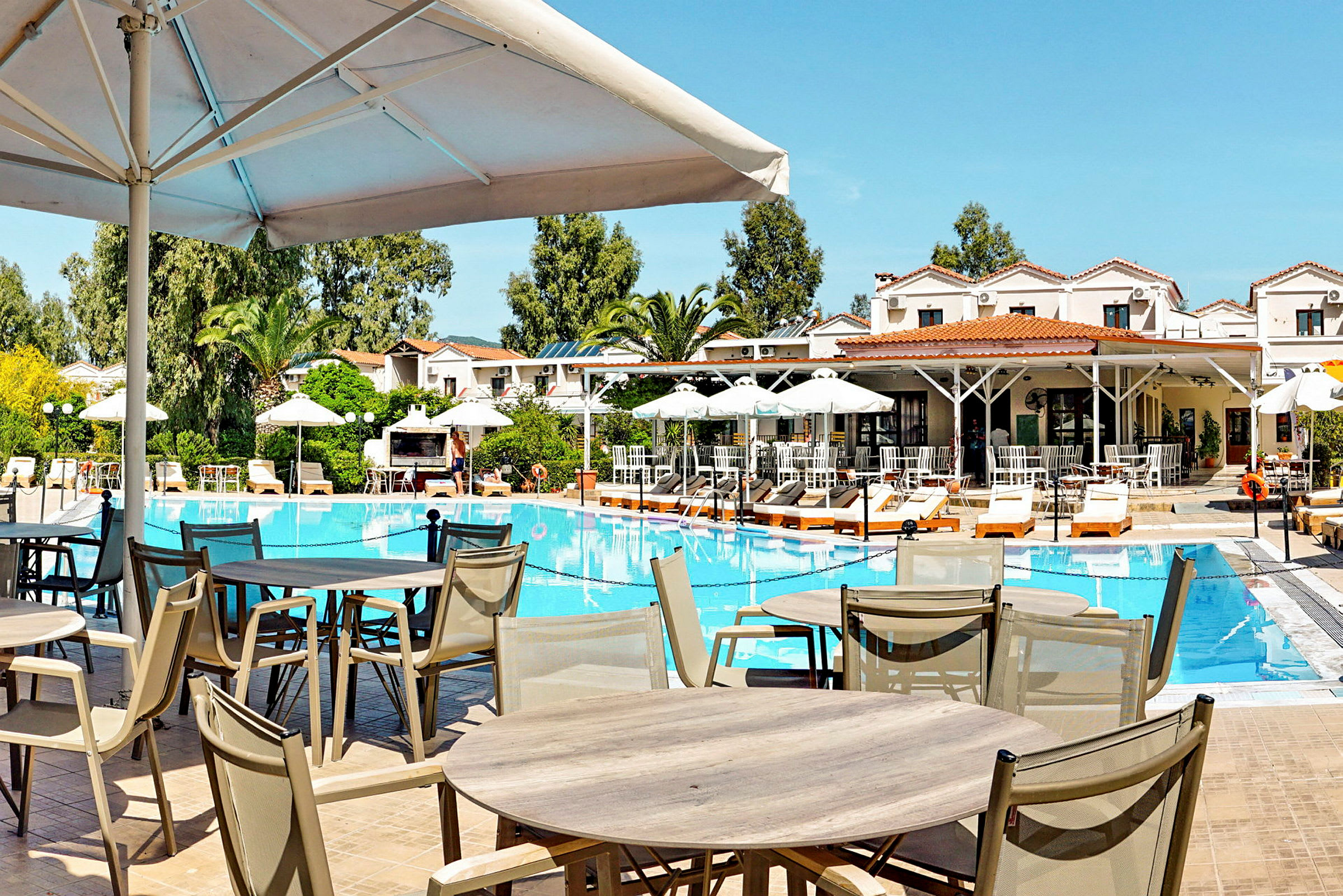Bild av en utomhuspool omgiven av solstolar och parasoller, med en restaurang byggnad i bakgrunden. (AI-genererad text)