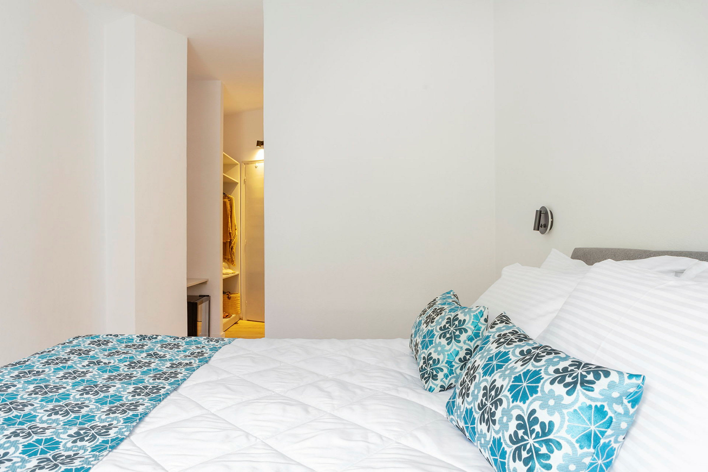 Ett hotellrum med en säng med vita sängkläder och mönstrade kuddar. I bakgrunden syns en garderob. (AI-genererad text)