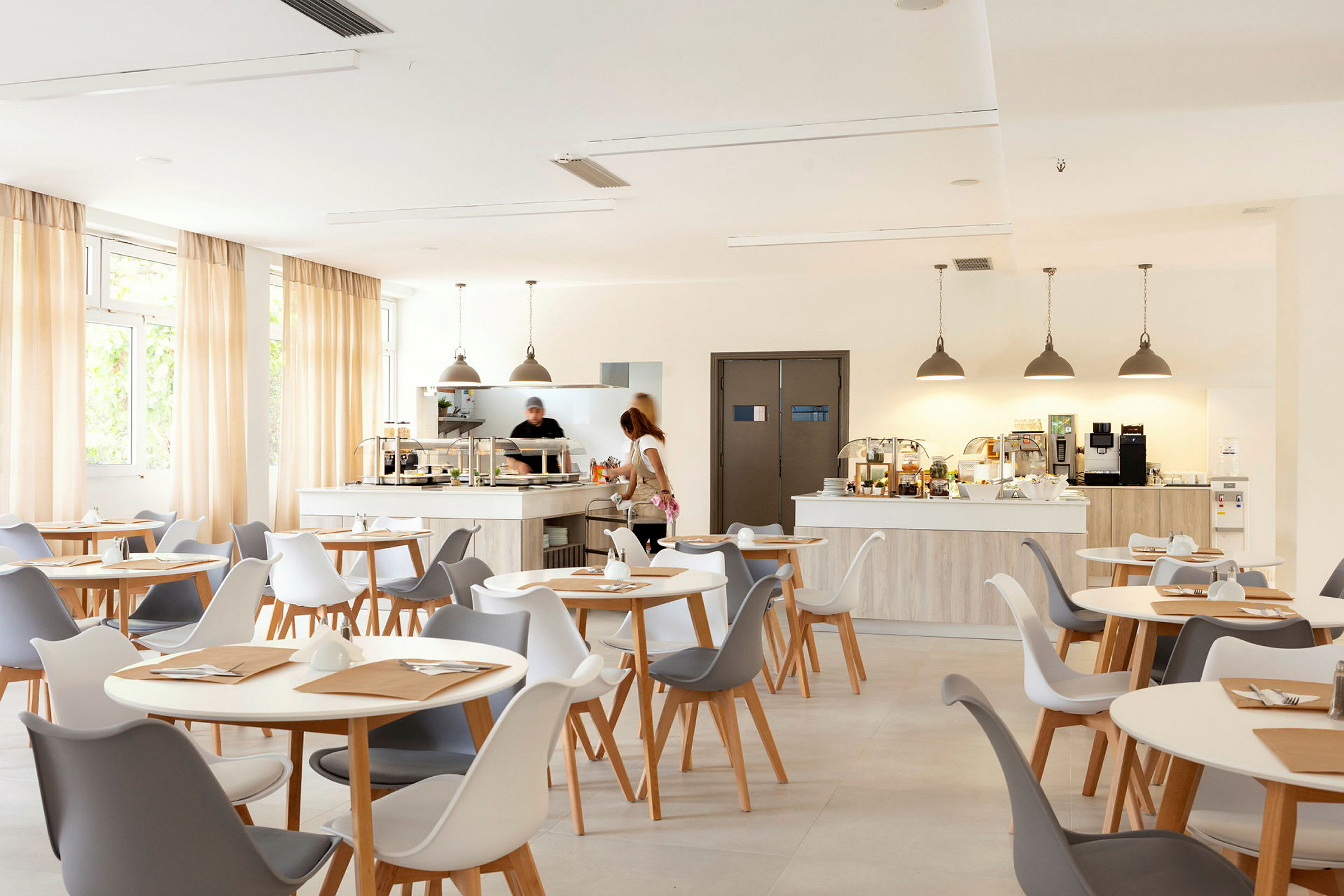 Ett ljust och modernt café med vita och gråa stolar samt ljus träinredning. (AI-genererad text)