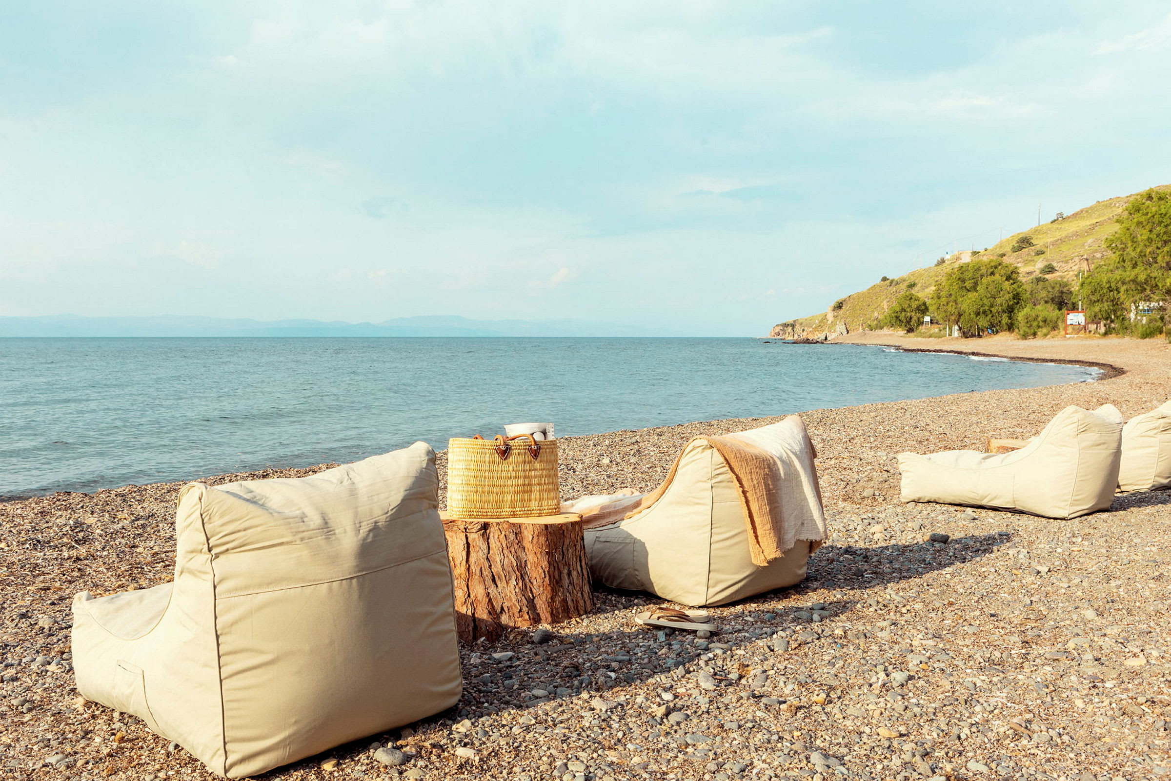 Fyra sittsäcks på en stenig strand bredvid en stubbe som fungerar som bord. (AI-genererad text)