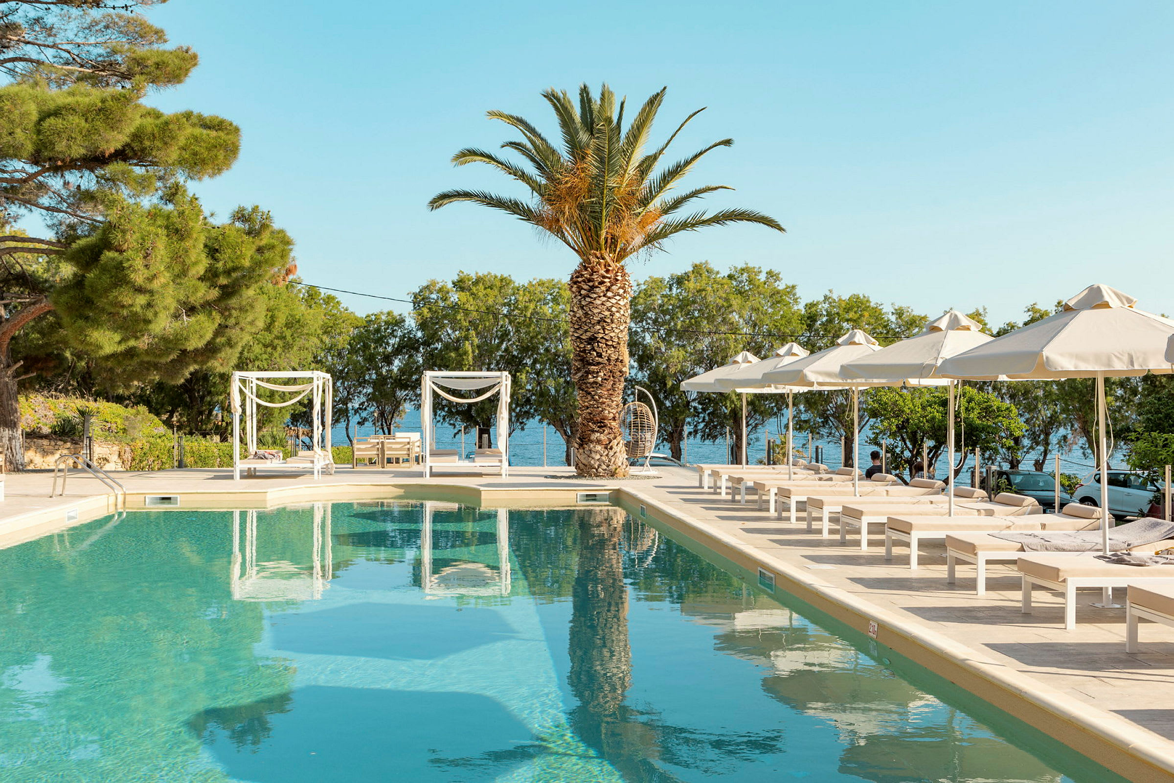 Pool med solstolar och parasoller, palmer och hav i bakgrunden. (AI-genererad text)