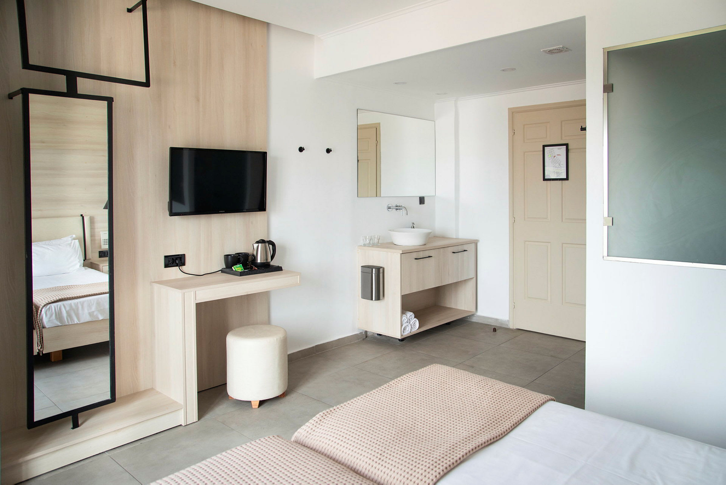 Modernt inrett hotellrum med bord, spegel, TV, säng och handfat. (AI-genererad text)