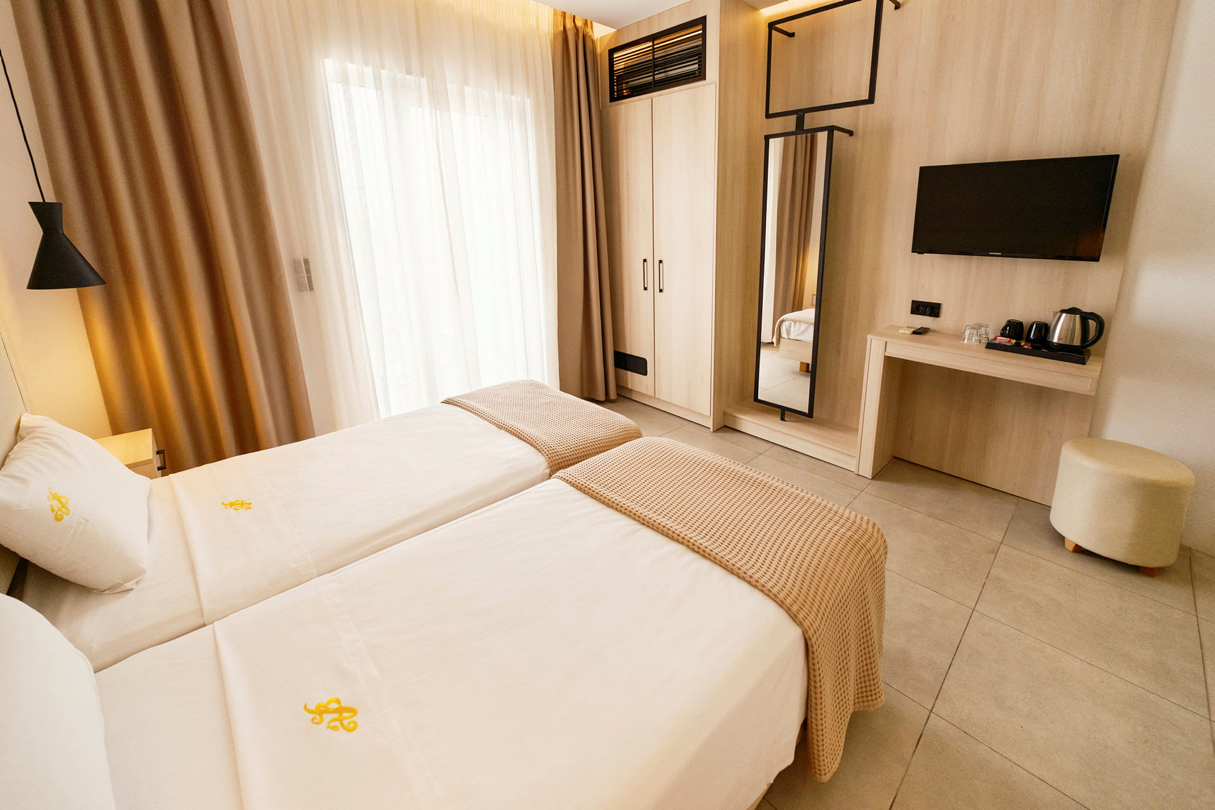 Hotellrum med två enkelsängar, en väggmonterad spegel, ett skrivbord och en TV. (AI-genererad text)