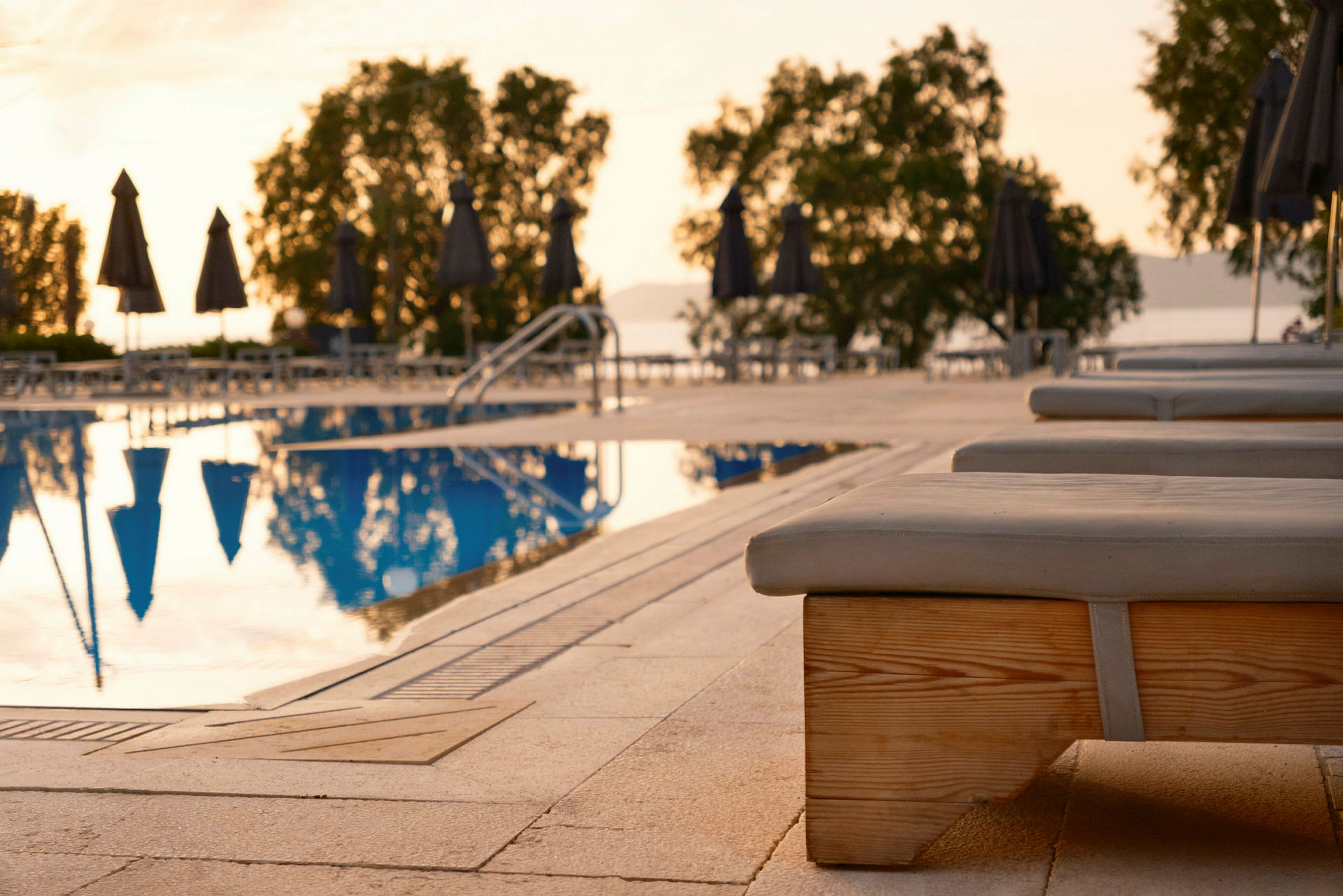 Solstolar vid en pool med parasoller och träd i bakgrunden. (AI-genererad text)