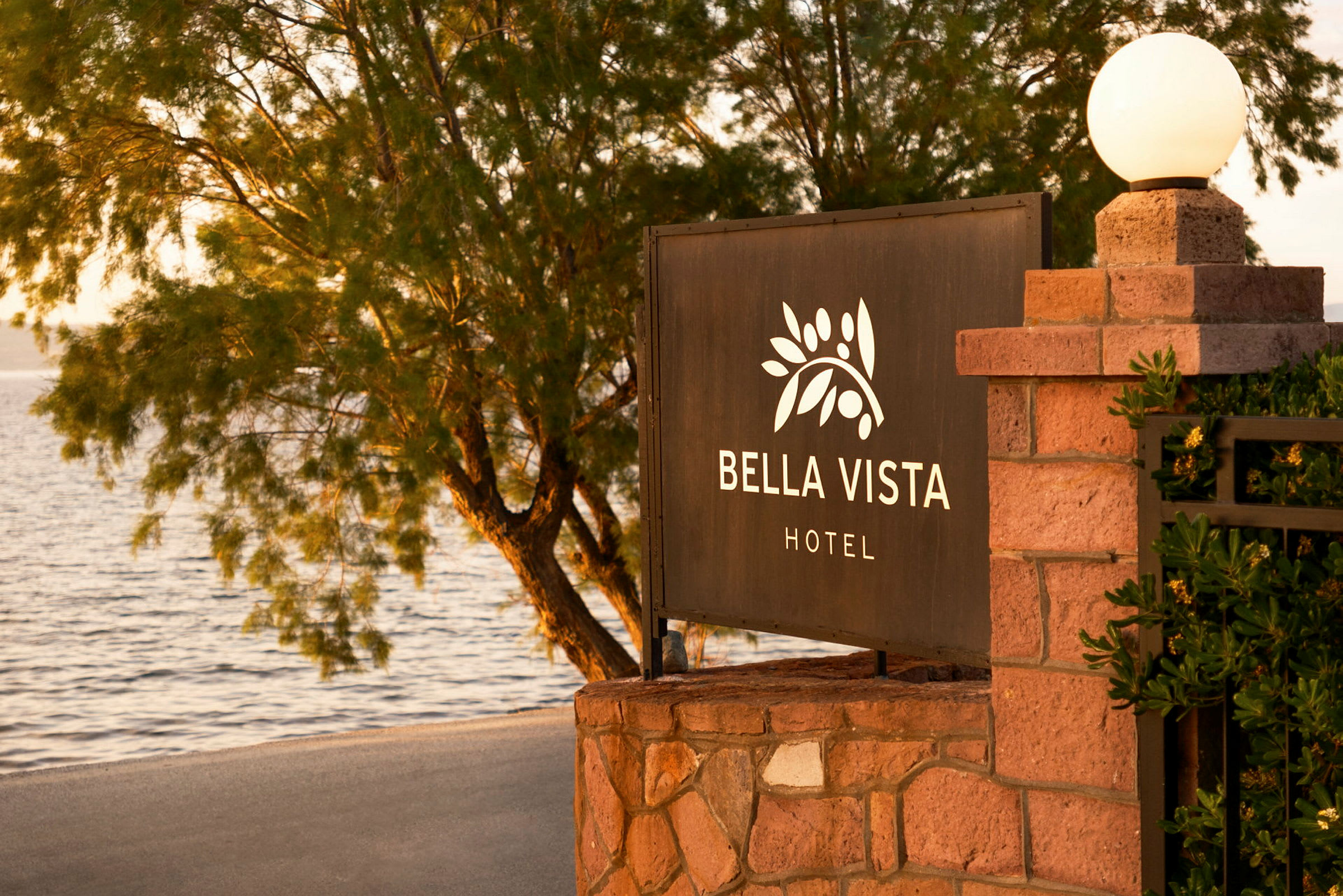 Skylt med texten "Bella Vista Hotel" vid en strand med träd i bakgrunden. (AI-genererad text)