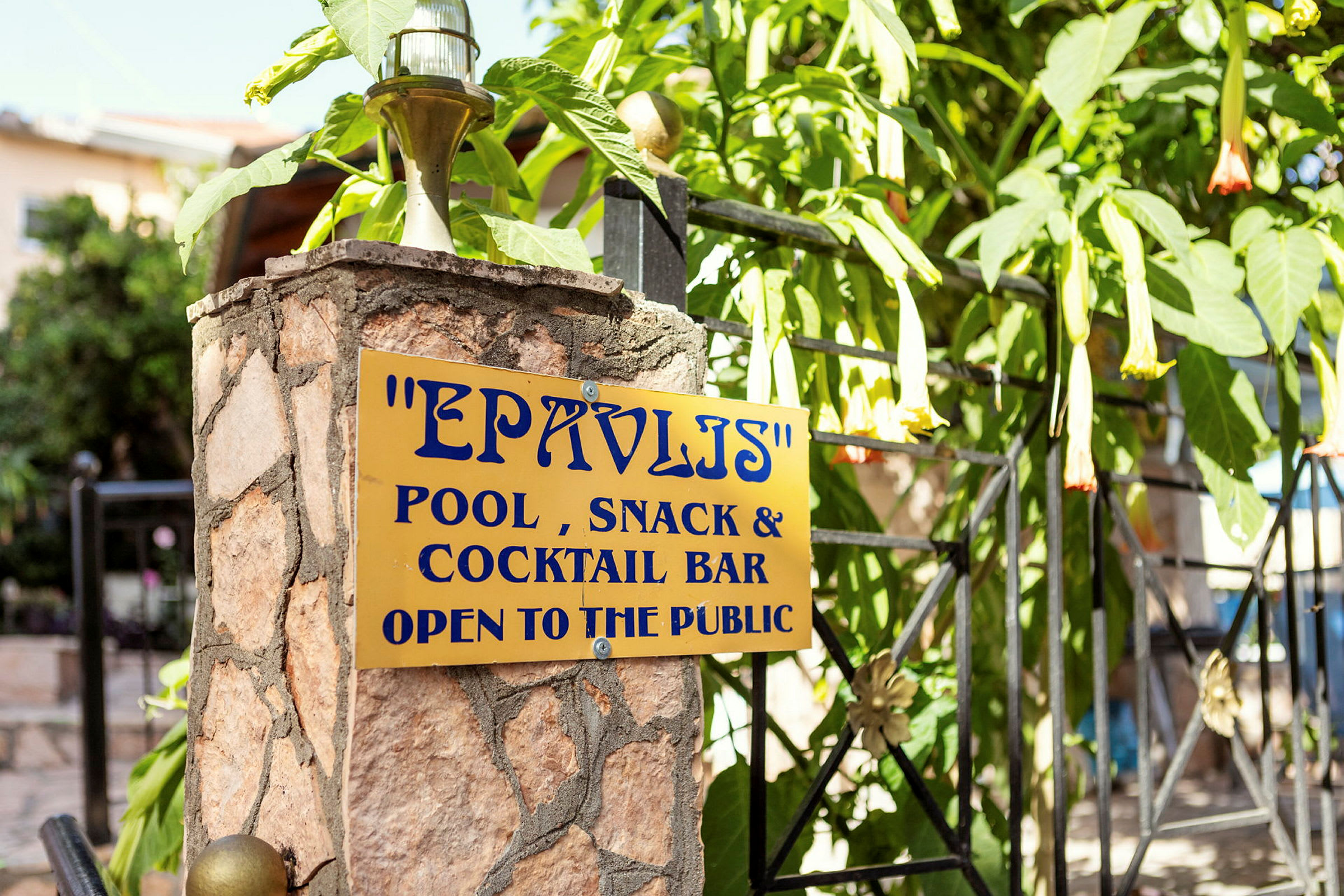 Skylt på en stenpelare med texten 'EPAVLIS Pool, Snack & Cocktail Bar Open to the public'. (AI-genererad text)