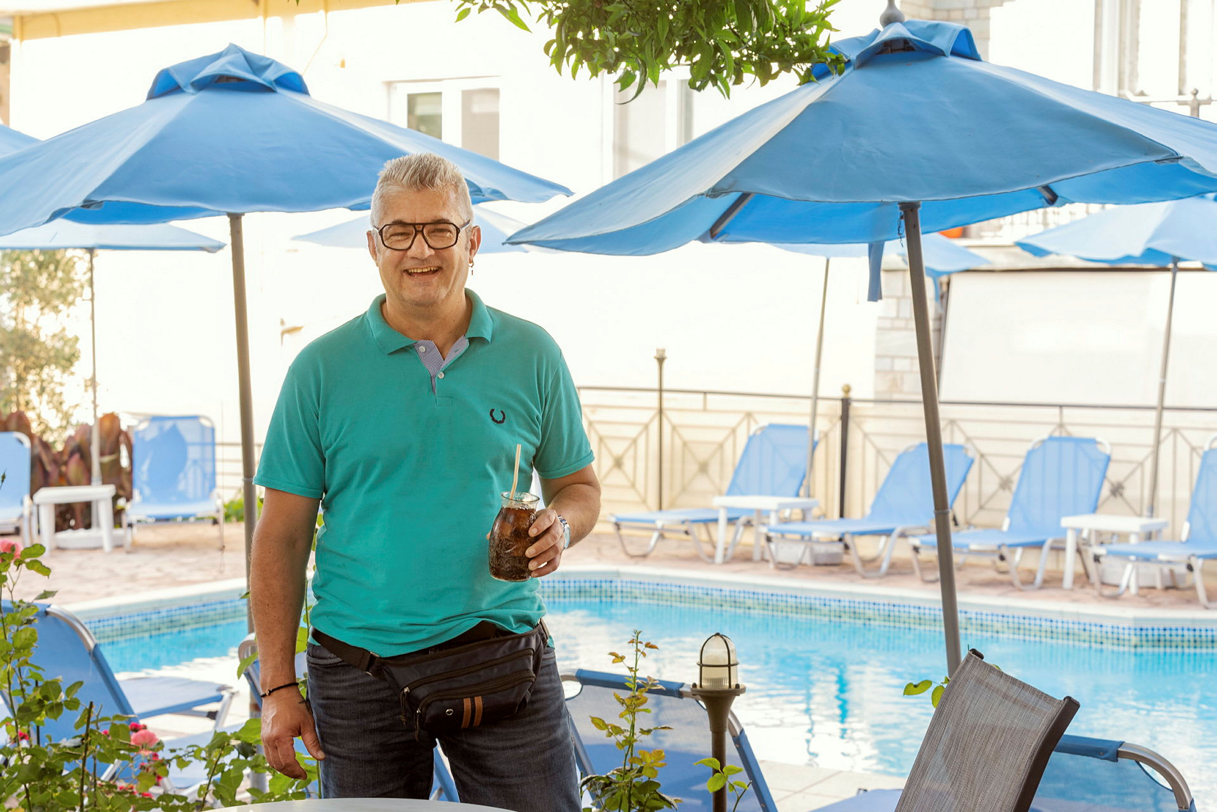 Person står framför en pool. Bakgrunden visar solstolar och parasoller. (AI-genererad text)
