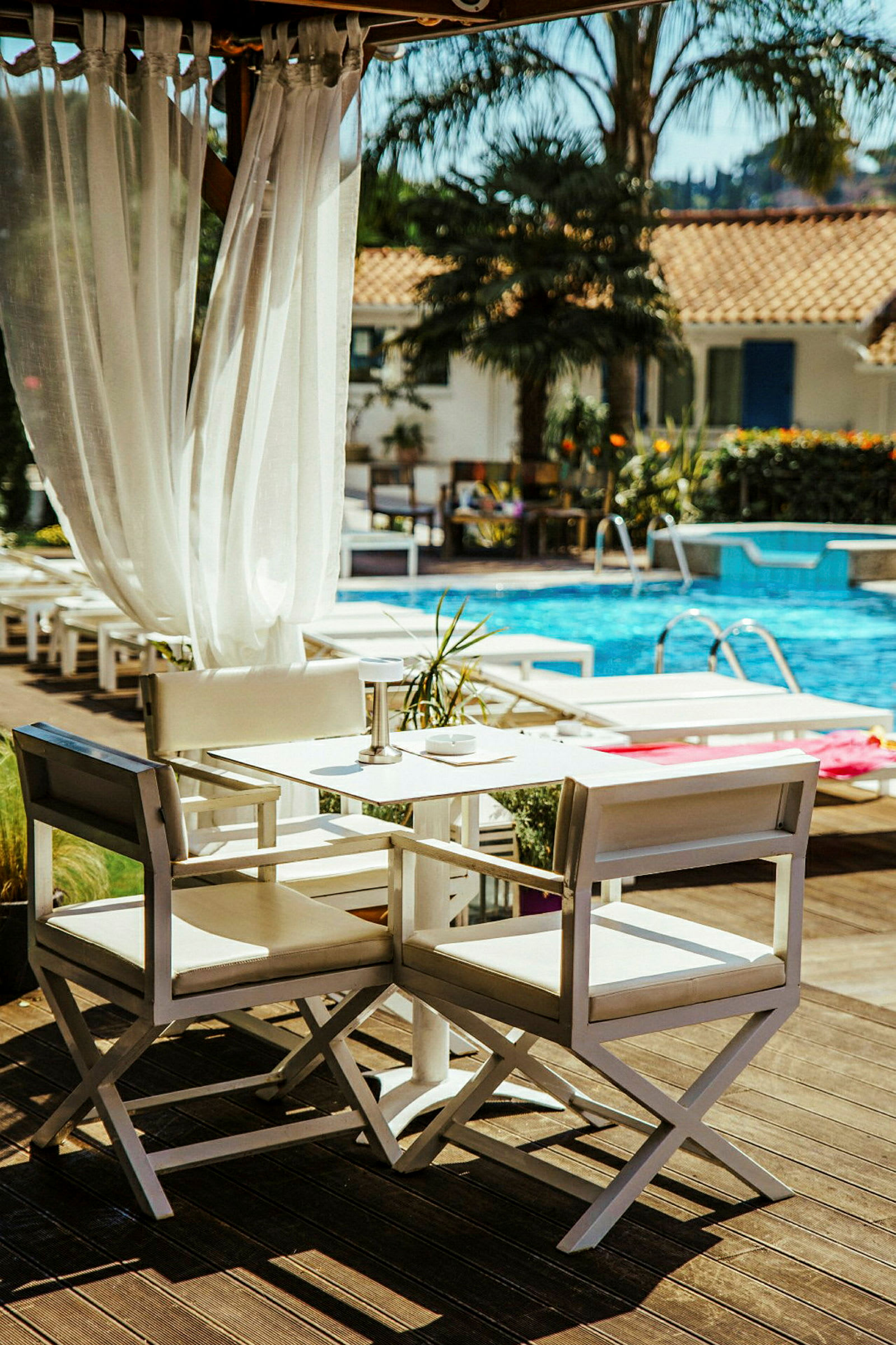 Ett bord med vita stolar nära en pool med palmer i bakgrunden. (AI-genererad text)